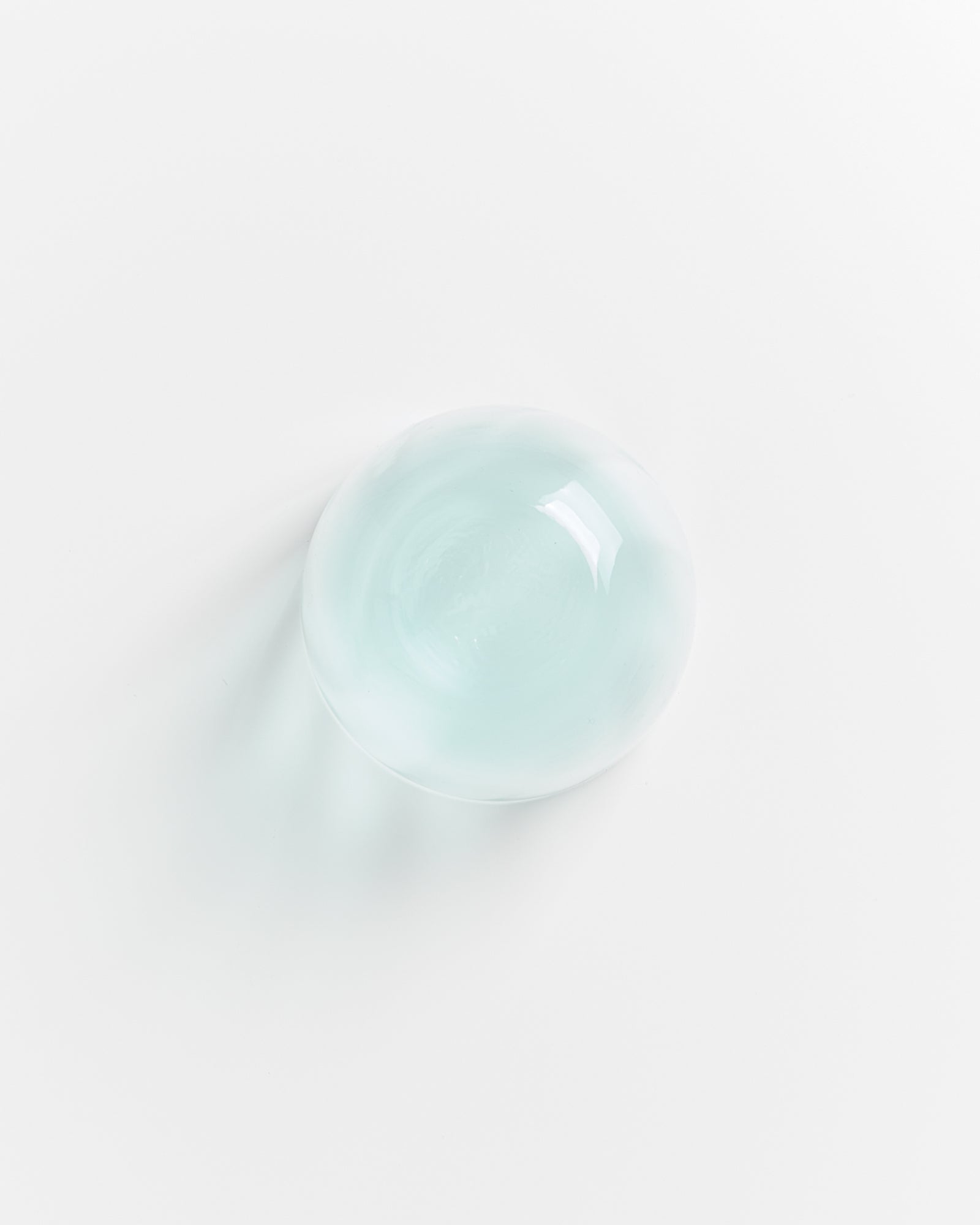 Glasklare Kugel liegt auf weißem Hintergrund mit leichter Lichtreflexion.