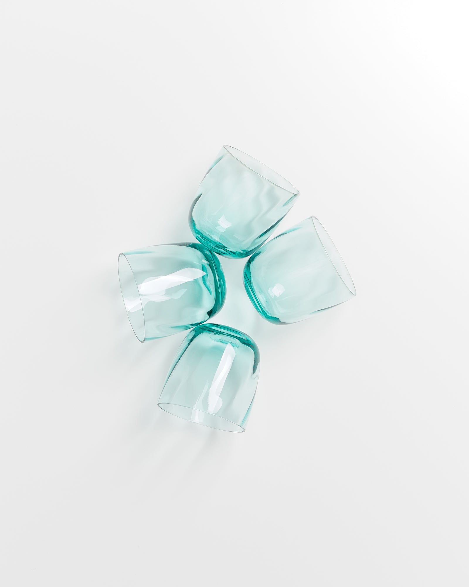 Vier türkisfarbene, leere Gläser liegen in einer kreuzförmigen Anordnung auf einer weißen Oberfläche.