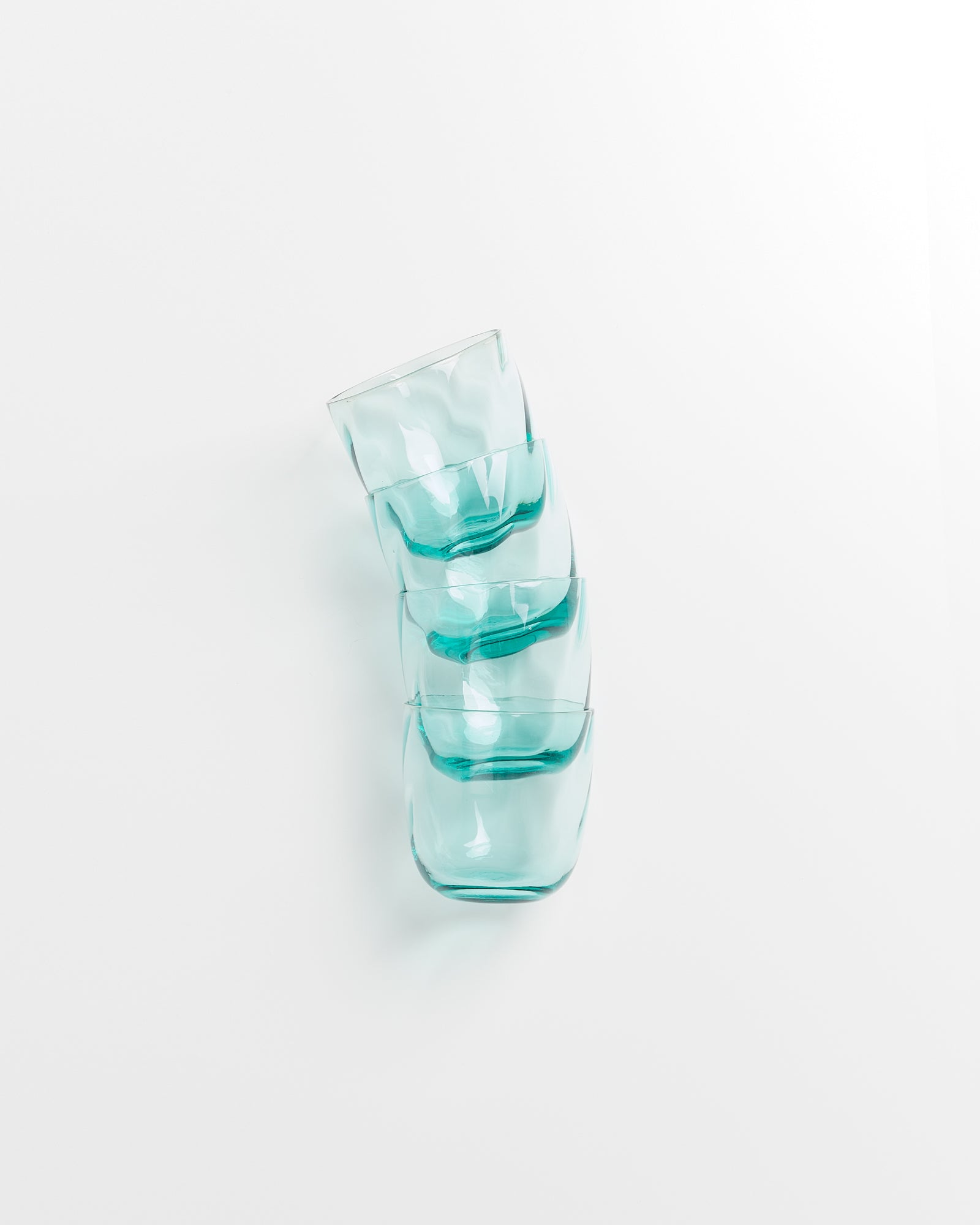 Vier türkisfarbene Gläser sind schräg übereinander gestapelt auf einem weißen Untergrund zu sehen.