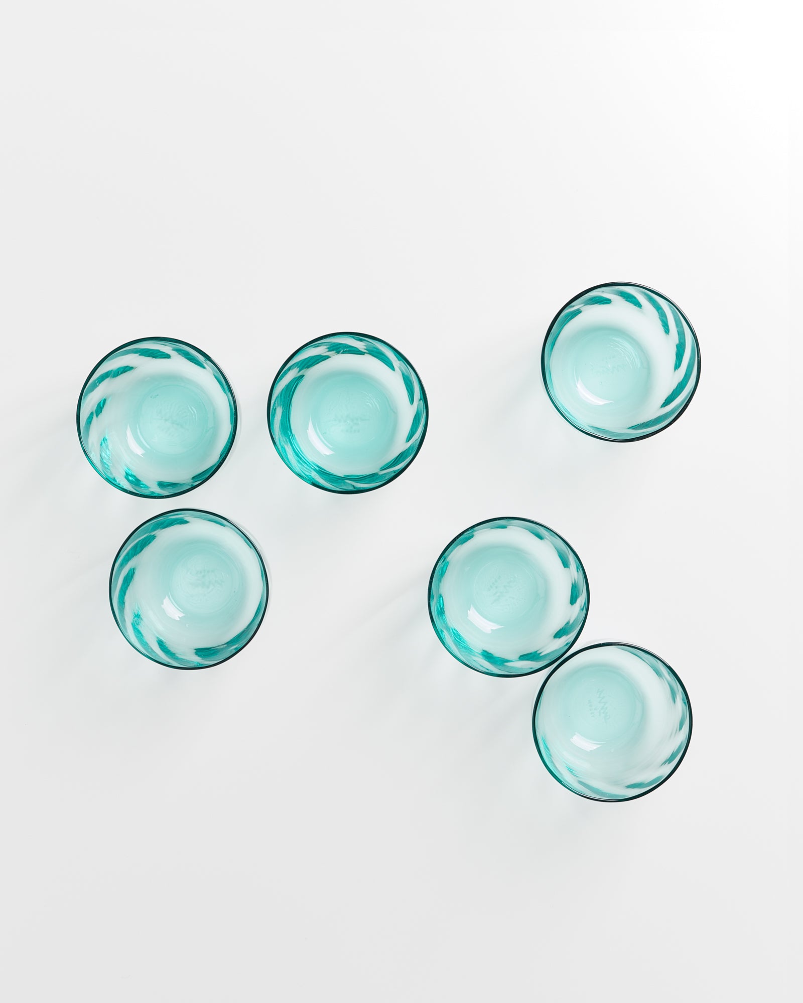 Sechs türkisfarbene Glasschalen auf einem weißen Hintergrund, im Sechseckmuster angeordnet.