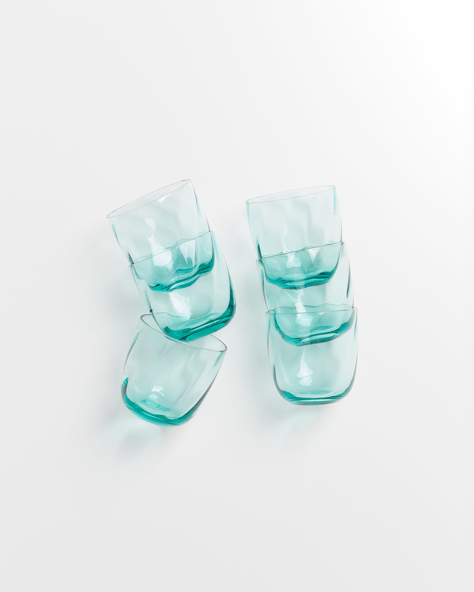 Sechs türkisfarbene Gläser sind kunstvoll auf einem weißen Hintergrund gestapelt.