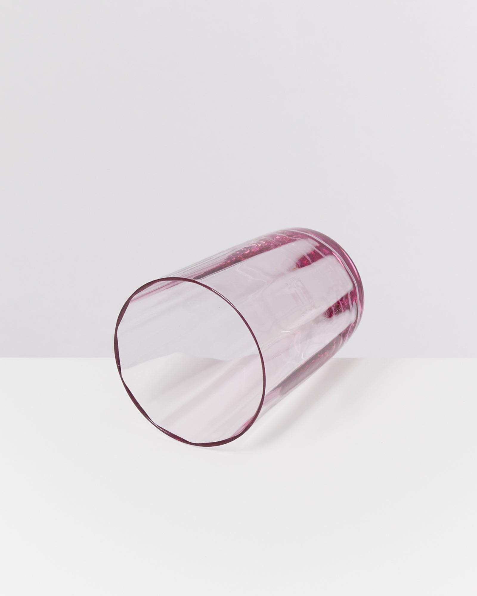 Liegendes, transparentes, pinkes Glas auf weißem Hintergrund.