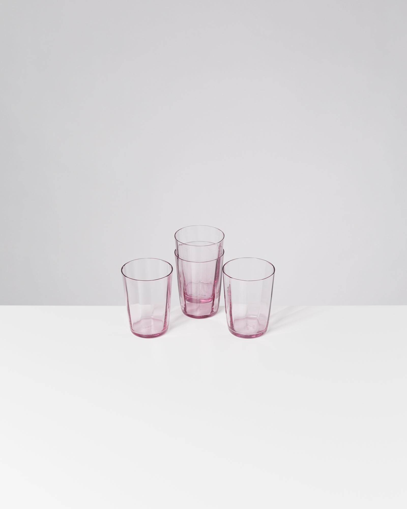 Vier rosafarbene Trinkgläser stehen auf einer weißen Oberfläche.