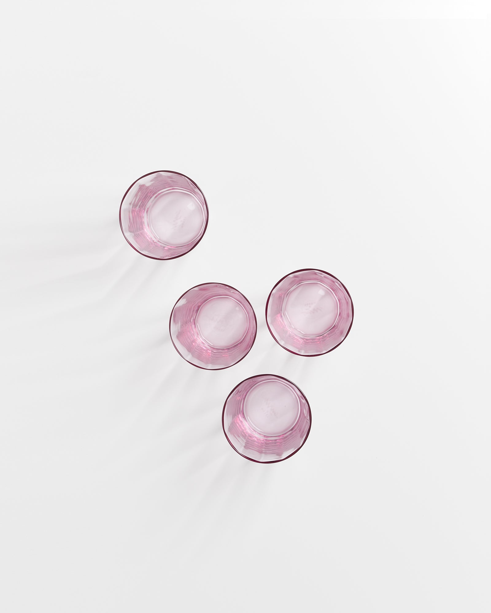 Vier rosafarbene Gläser stehen auf einer weißen Oberfläche in einem quadratischen Muster.