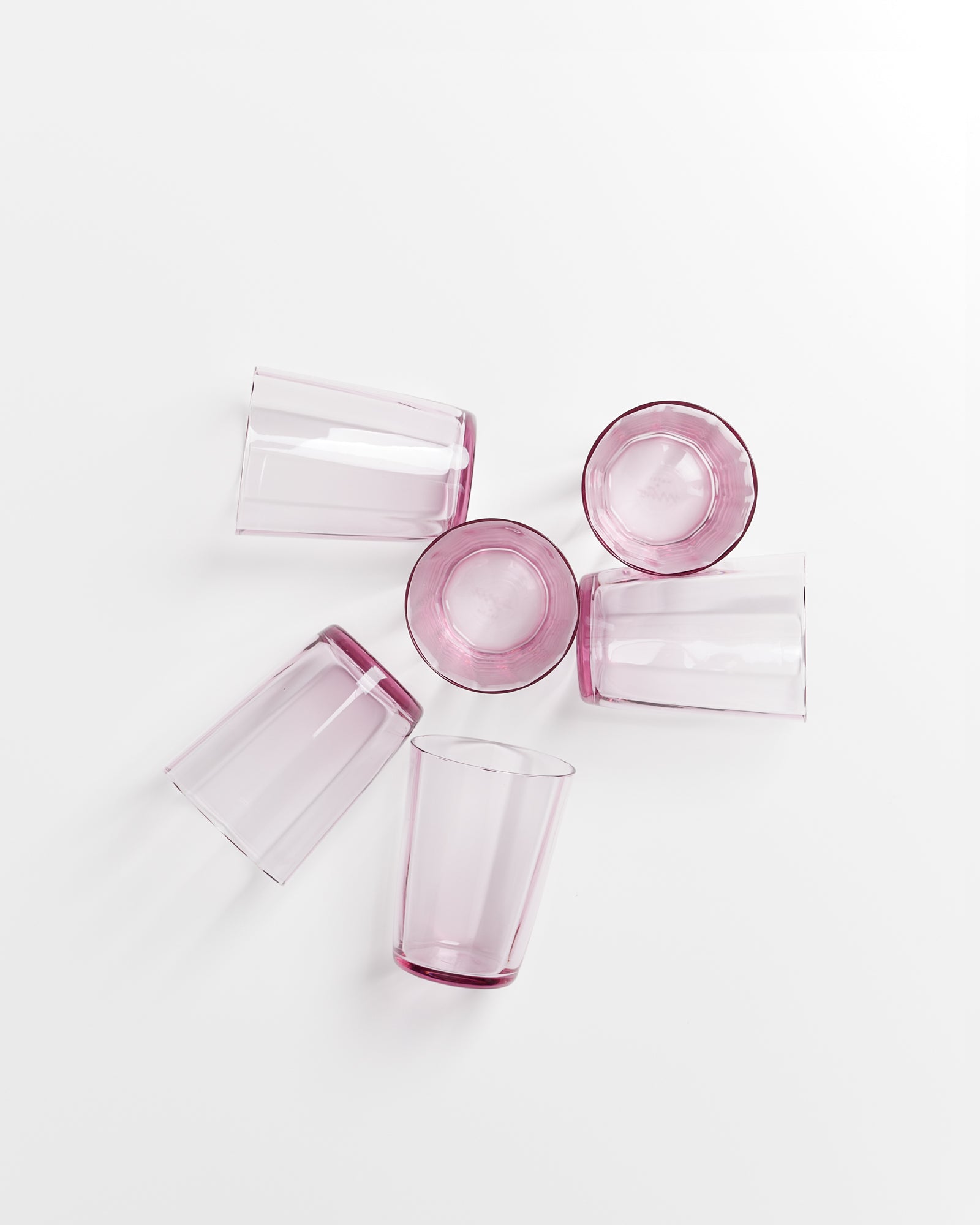 Fünf rosafarbene Gläser liegen und stehen auf einer weißen Oberfläche in unterschiedlichen Positionen.