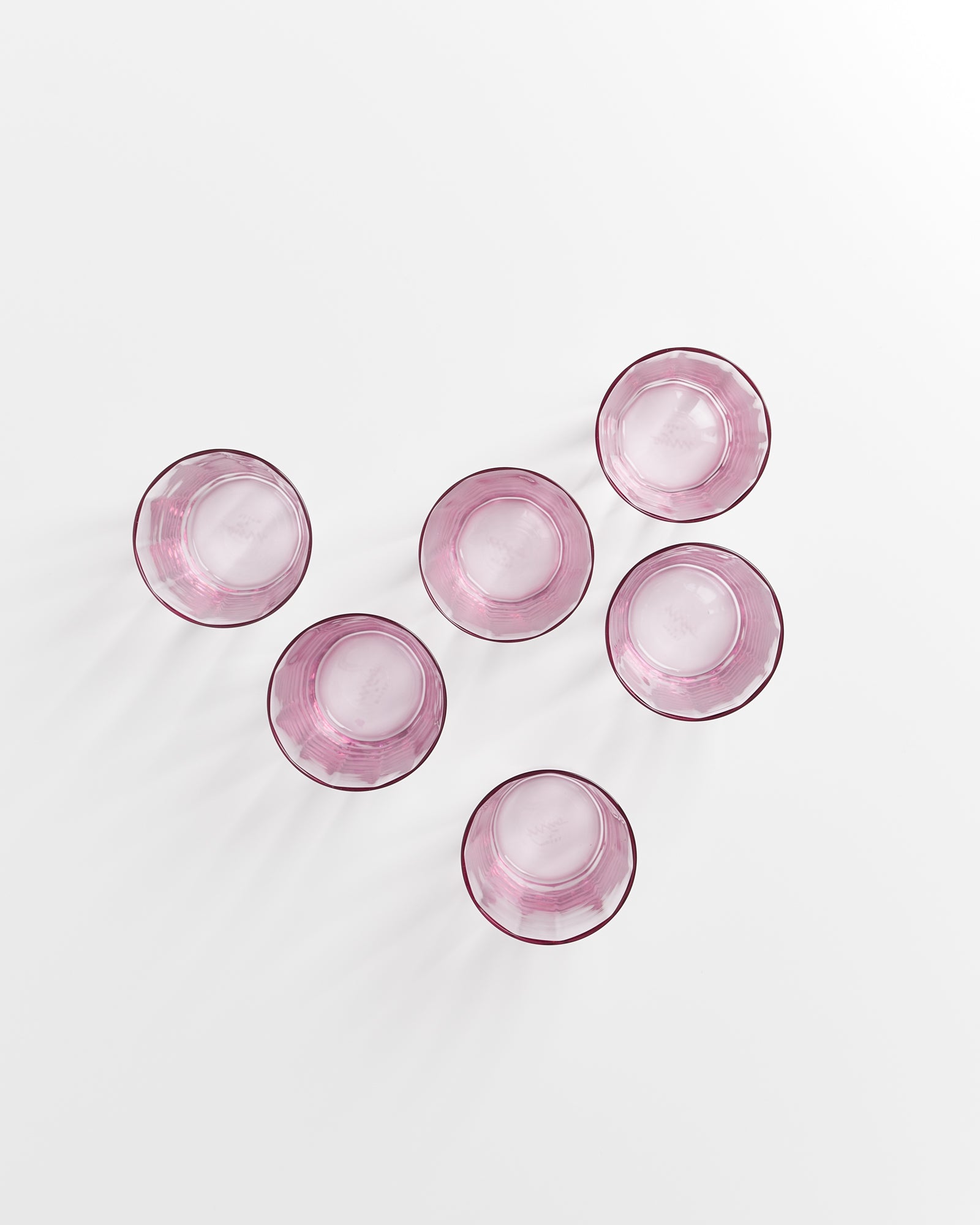 Sechs rosafarbene Gläser stehen auf einem weißen Hintergrund in zwei Reihen.