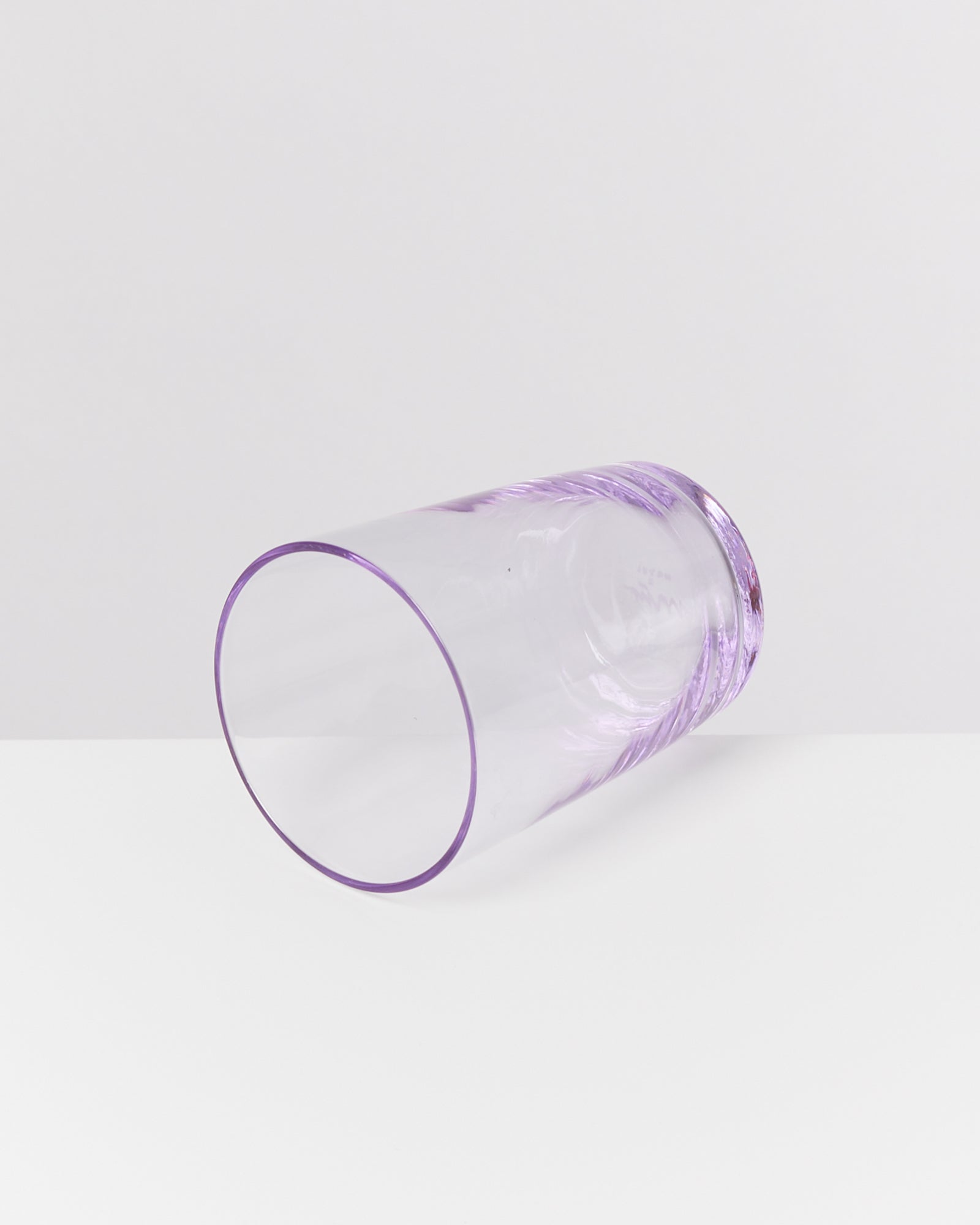 Ein durchsichtiges, lila Glas liegt auf der Seite auf einer weißen Oberfläche.