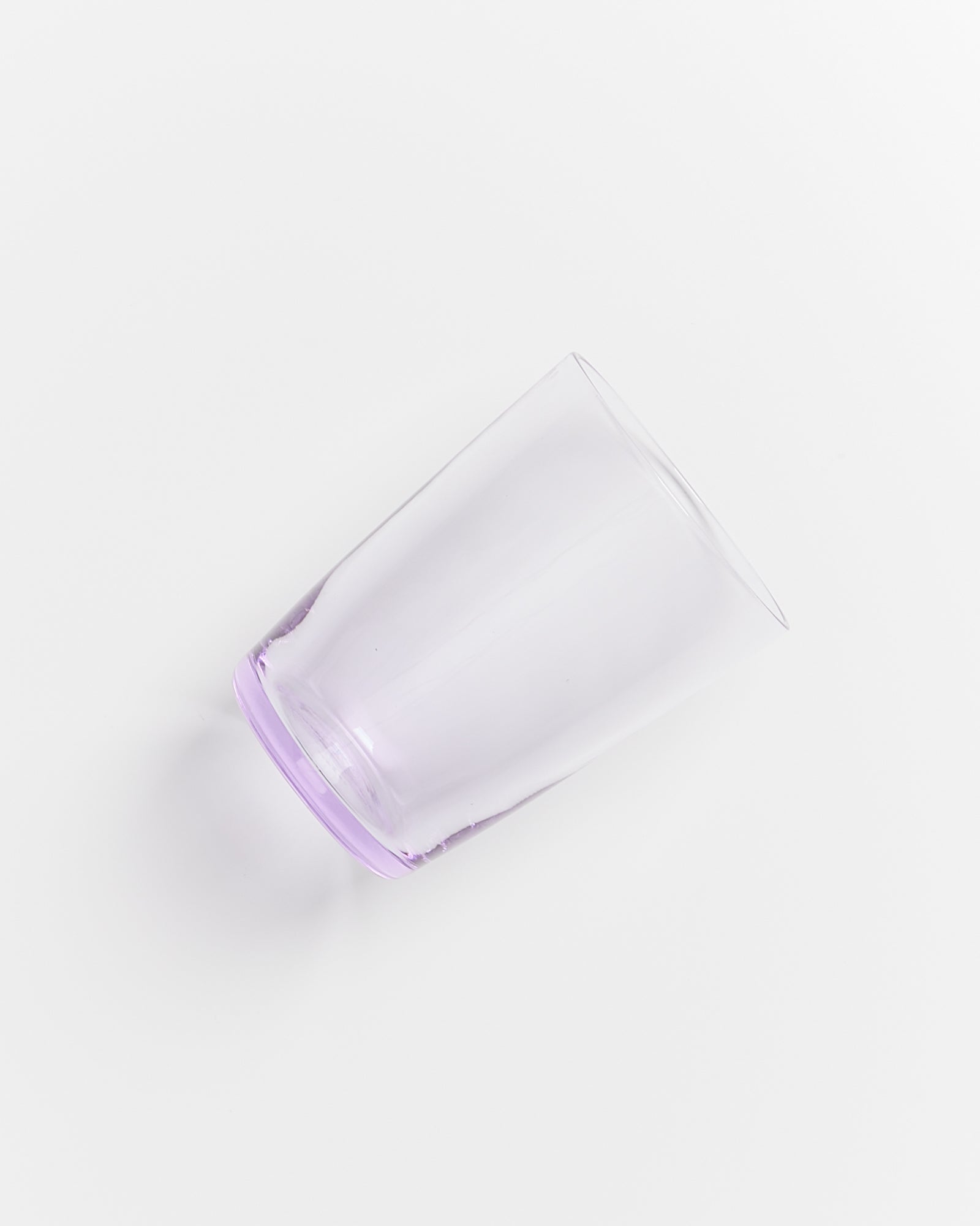 Ein durchsichtiges Glas mit leicht violettem Rand liegt auf einer weißen Oberfläche.
