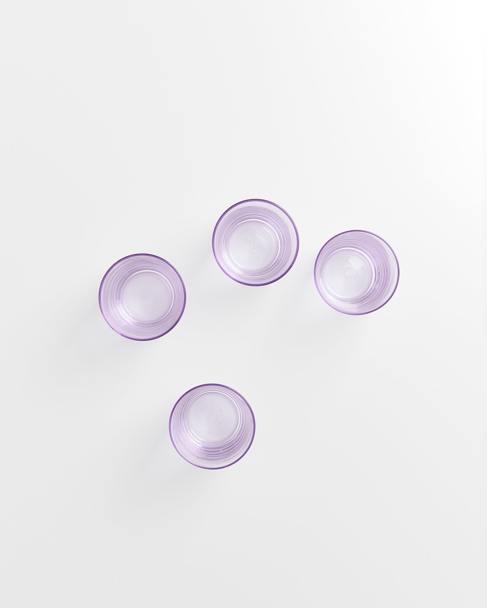 Vier lila Gläser auf weißem Hintergrund, aus der Vogelperspektive angeordnet.
