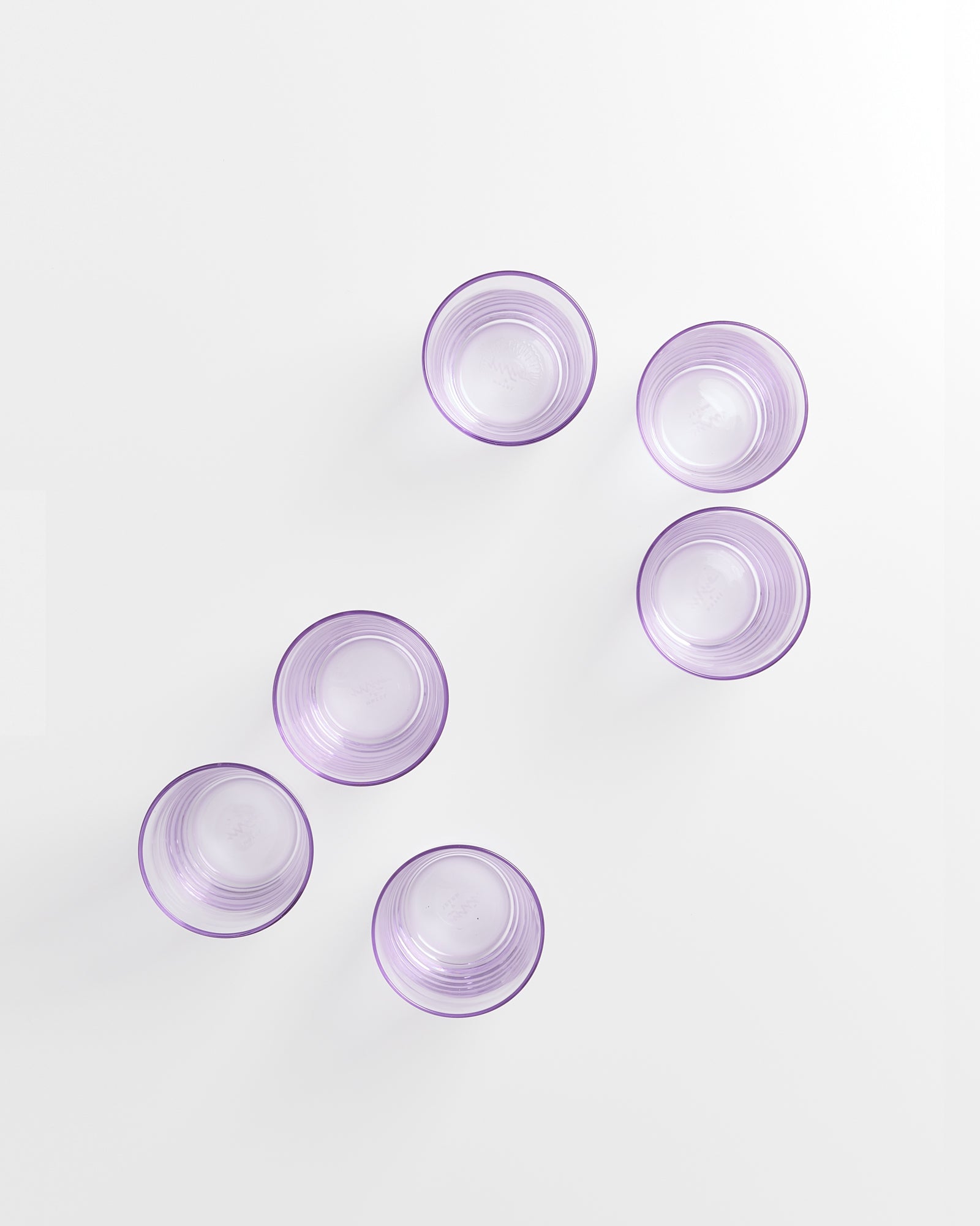 Sechs lila Gläser sind gleichmäßig auf einer weißen Oberfläche verteilt.