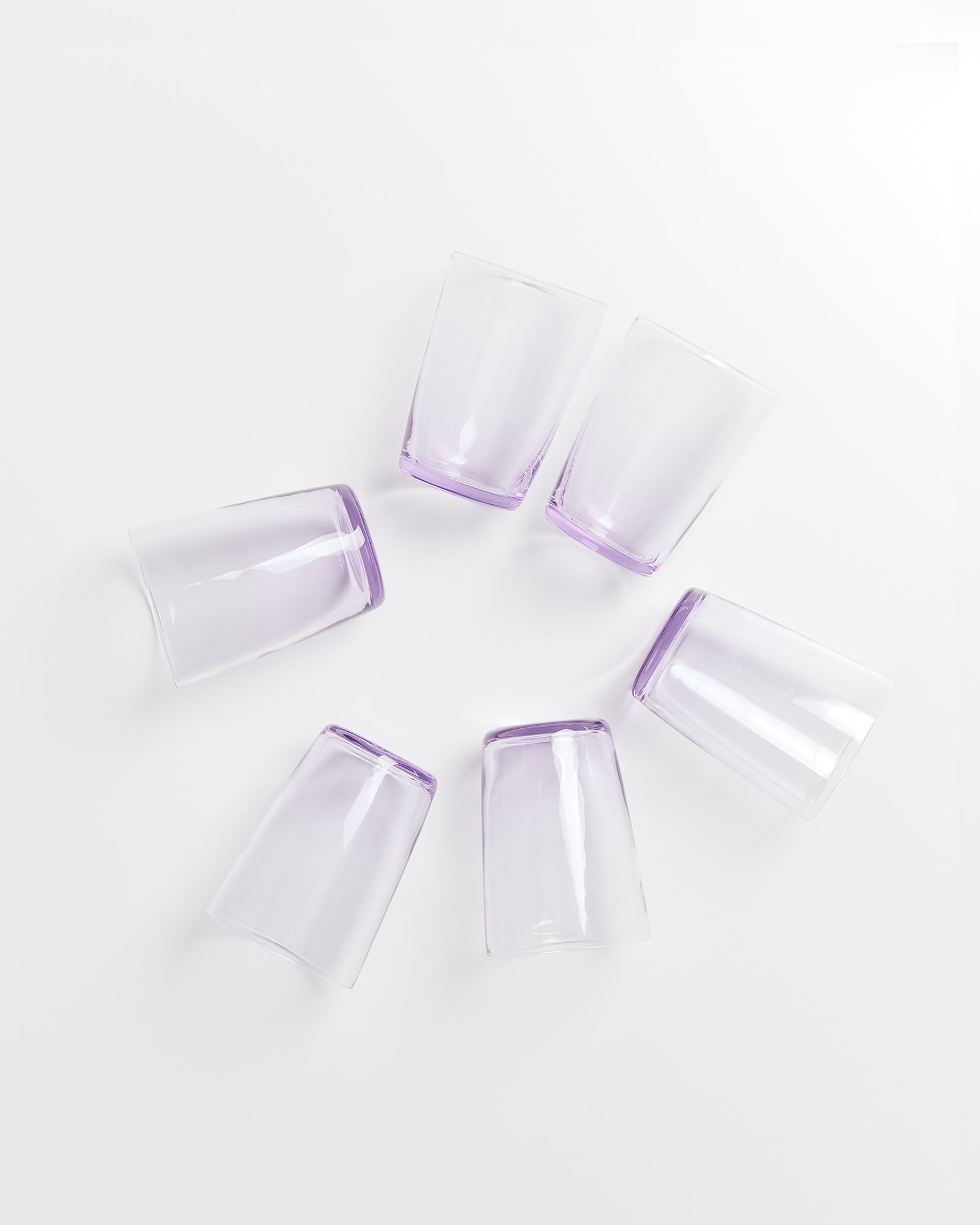 Sechs transparente, lilafarbene Gläser sind auf einer weißen Oberfläche in einem Kreis angeordnet.