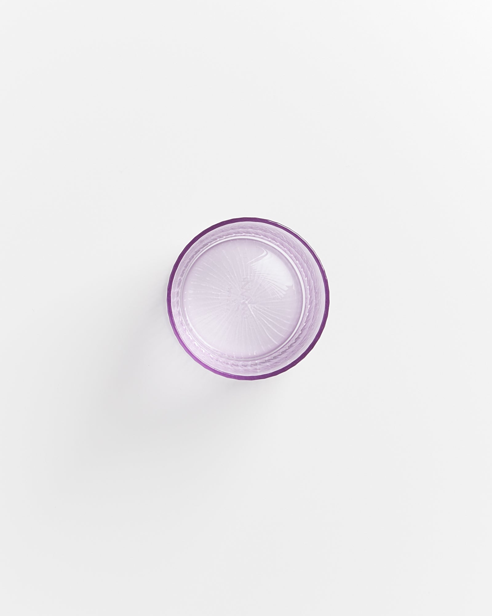 Lila Glas mit strukturiertem Boden auf weißem Hintergrund, von oben fotografiert.