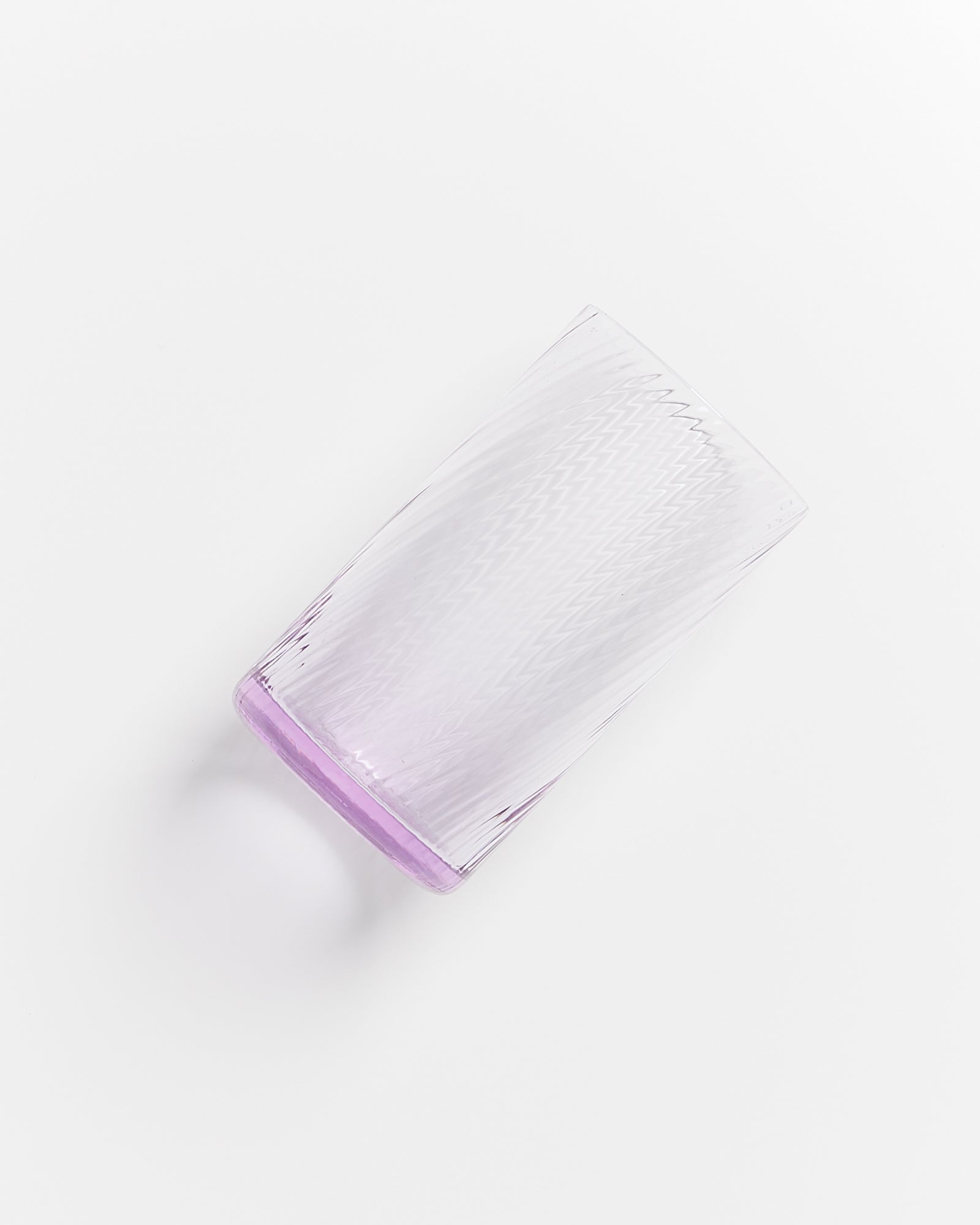 Durchsichtiges Glas mit leicht lila Boden auf weißem Hintergrund liegend, mit einem feinen Zickzackmuster.