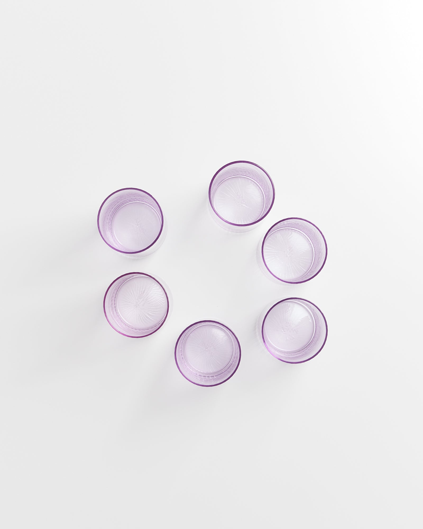 Sechs lila Gläser stehen in einem Kreis auf einer weißen Fläche.