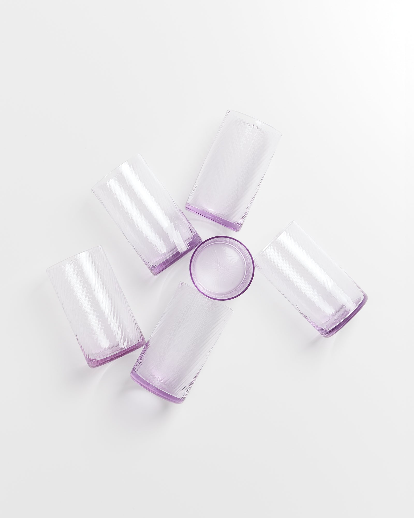 Fünf lila Glasbecher liegen auf weißem Hintergrund in sternförmiger Anordnung.