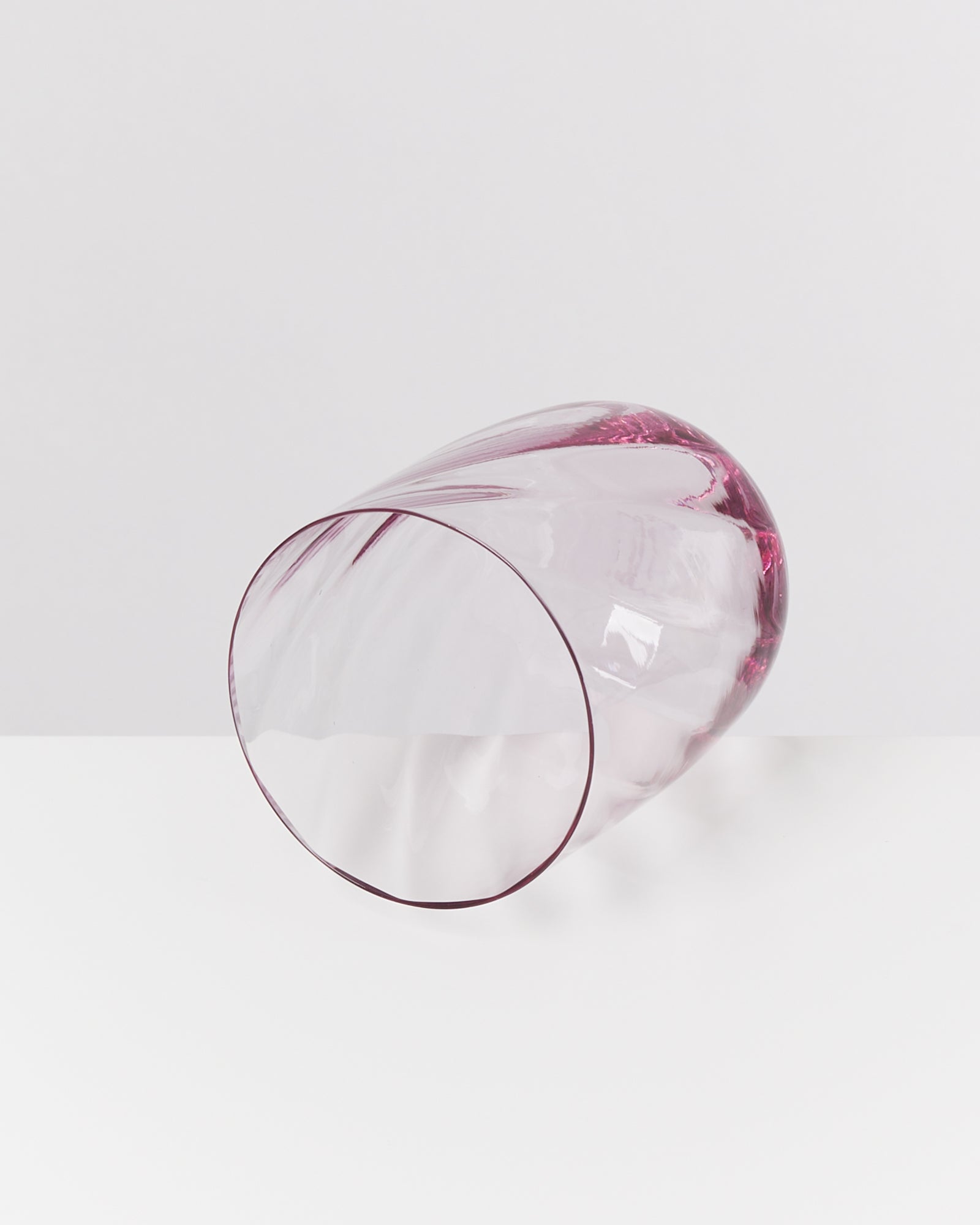 Rosa, durchsichtige Vase liegt auf der Seite auf einem weißen Hintergrund.