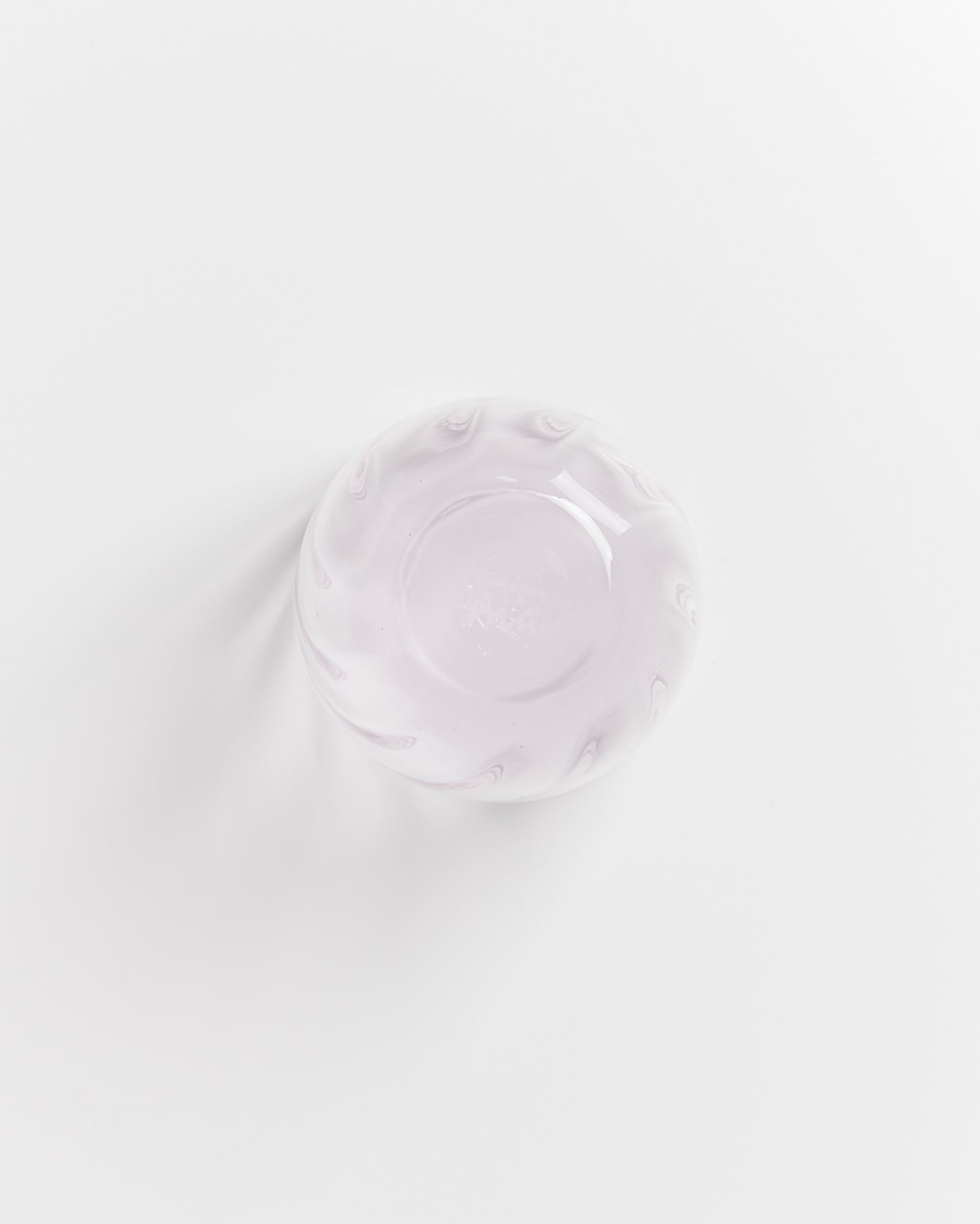Runde, milchig-rosa Glasschale mit wellenförmigem Rand auf weißem Hintergrund, von oben fotografiert.