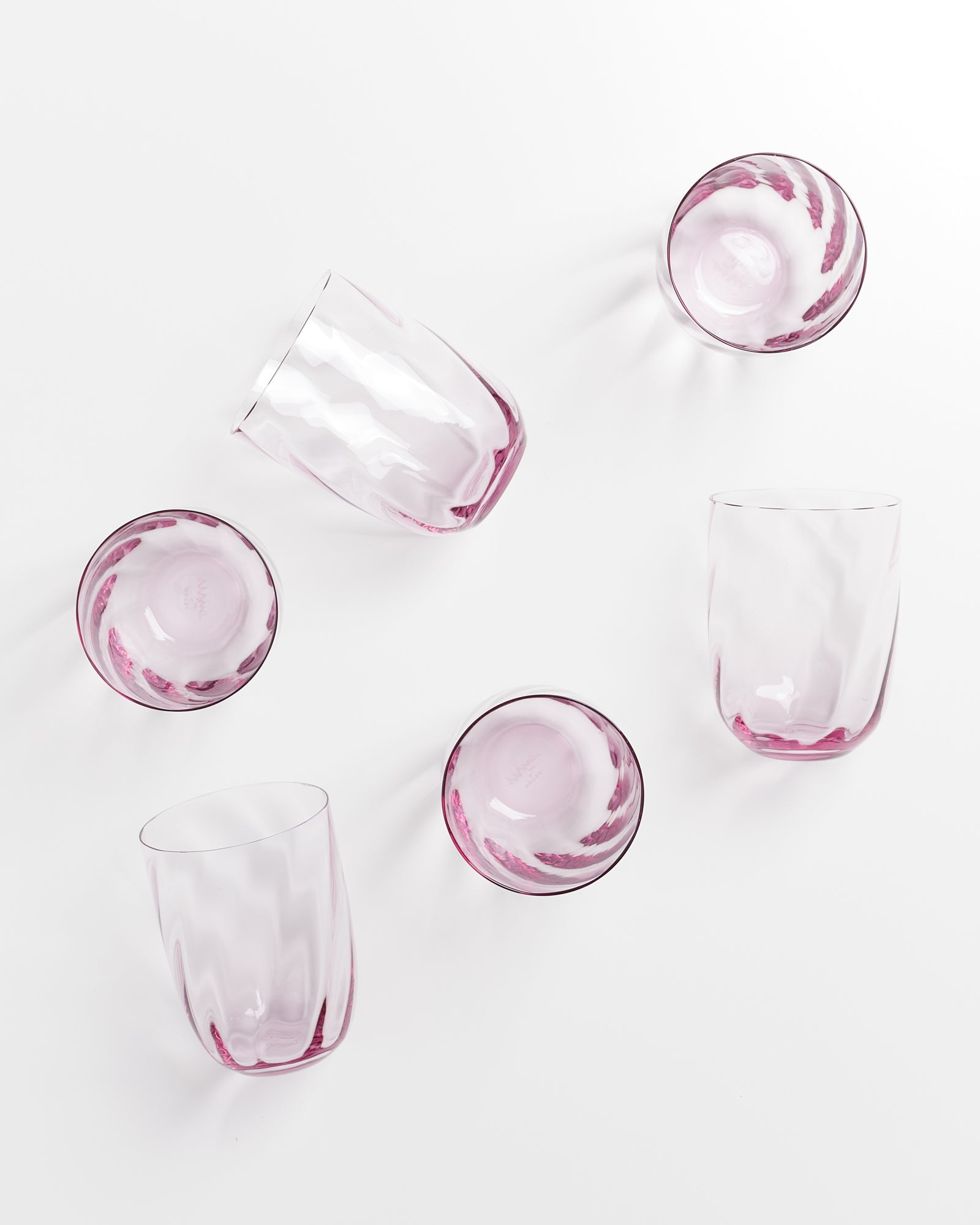 Sechs rosa Gläser in verschiedenen Winkeln auf einer weißen Oberfläche angeordnet.