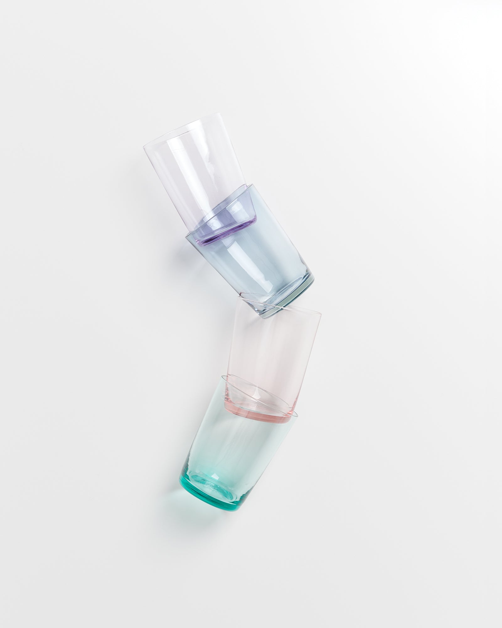 Vier farbige Gläser sind gestapelt und leicht gekippt auf einer weißen Oberfläche zu sehen.