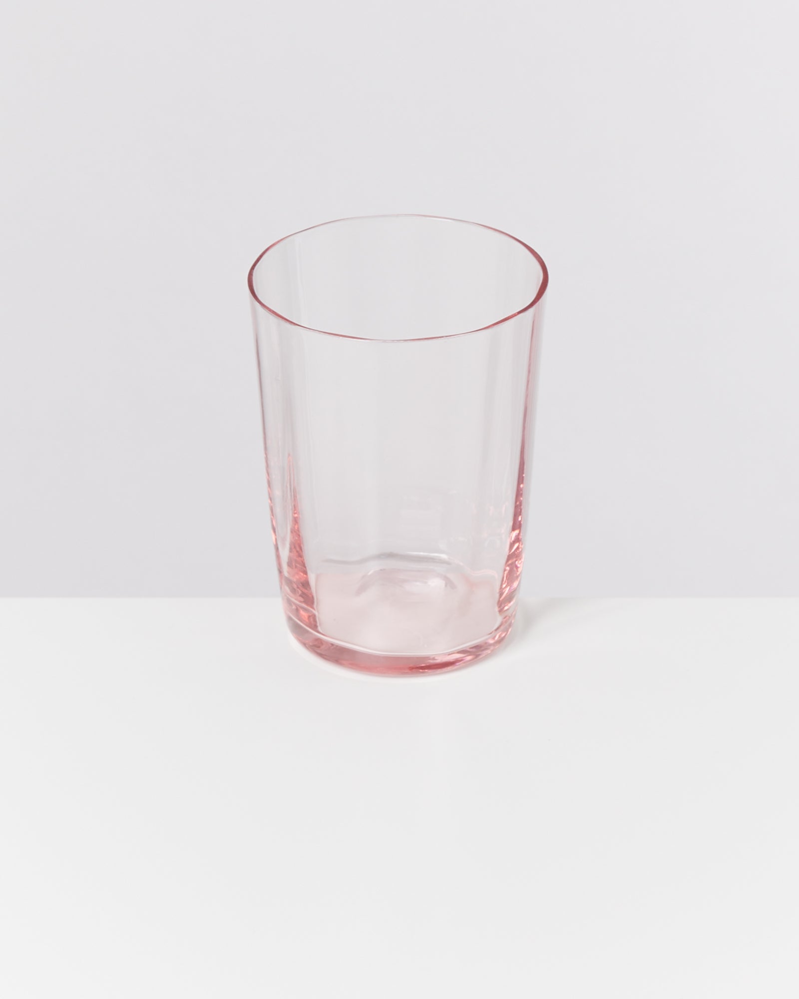 Ein durchsichtiges rosafarbenes Glas steht auf einem weißen Hintergrund.