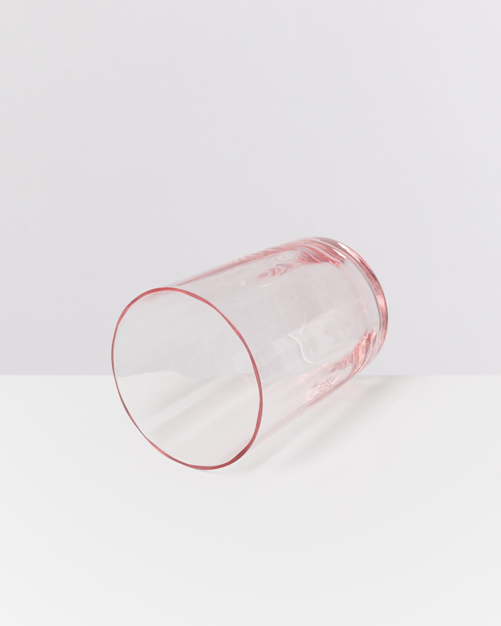 Ein rosa, durchscheinendes Glas liegt auf der Seite auf einer weißen Oberfläche.