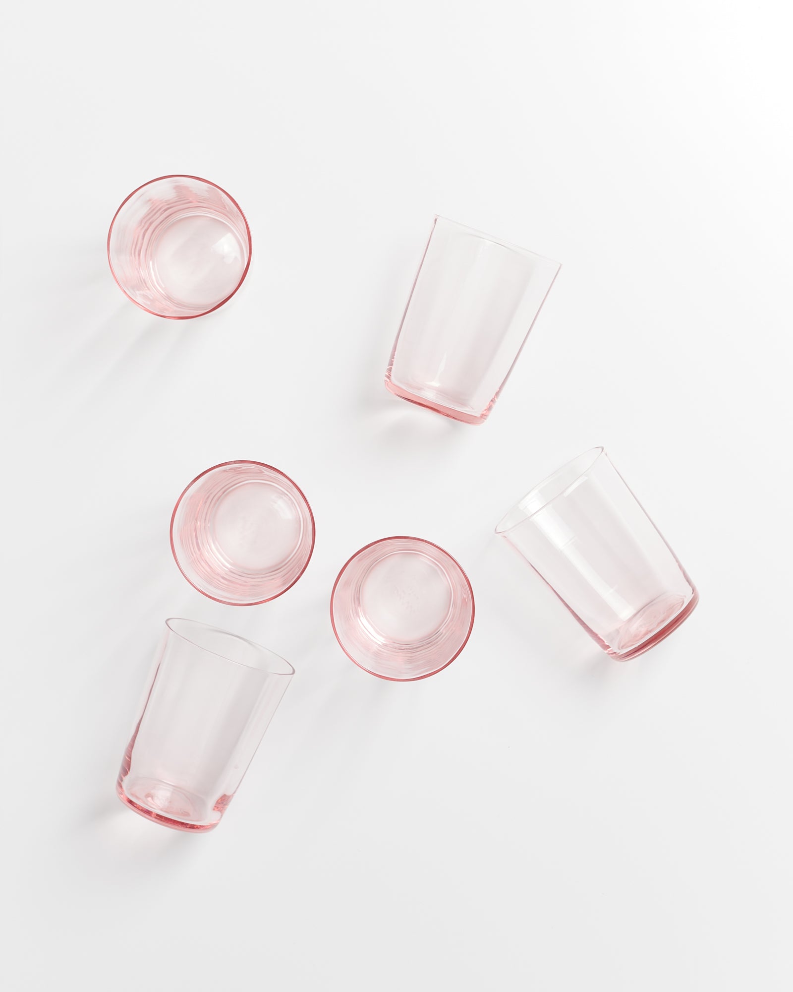 Fünf rosafarbene Gläser liegen auf einem weißen Hintergrund verteilt.