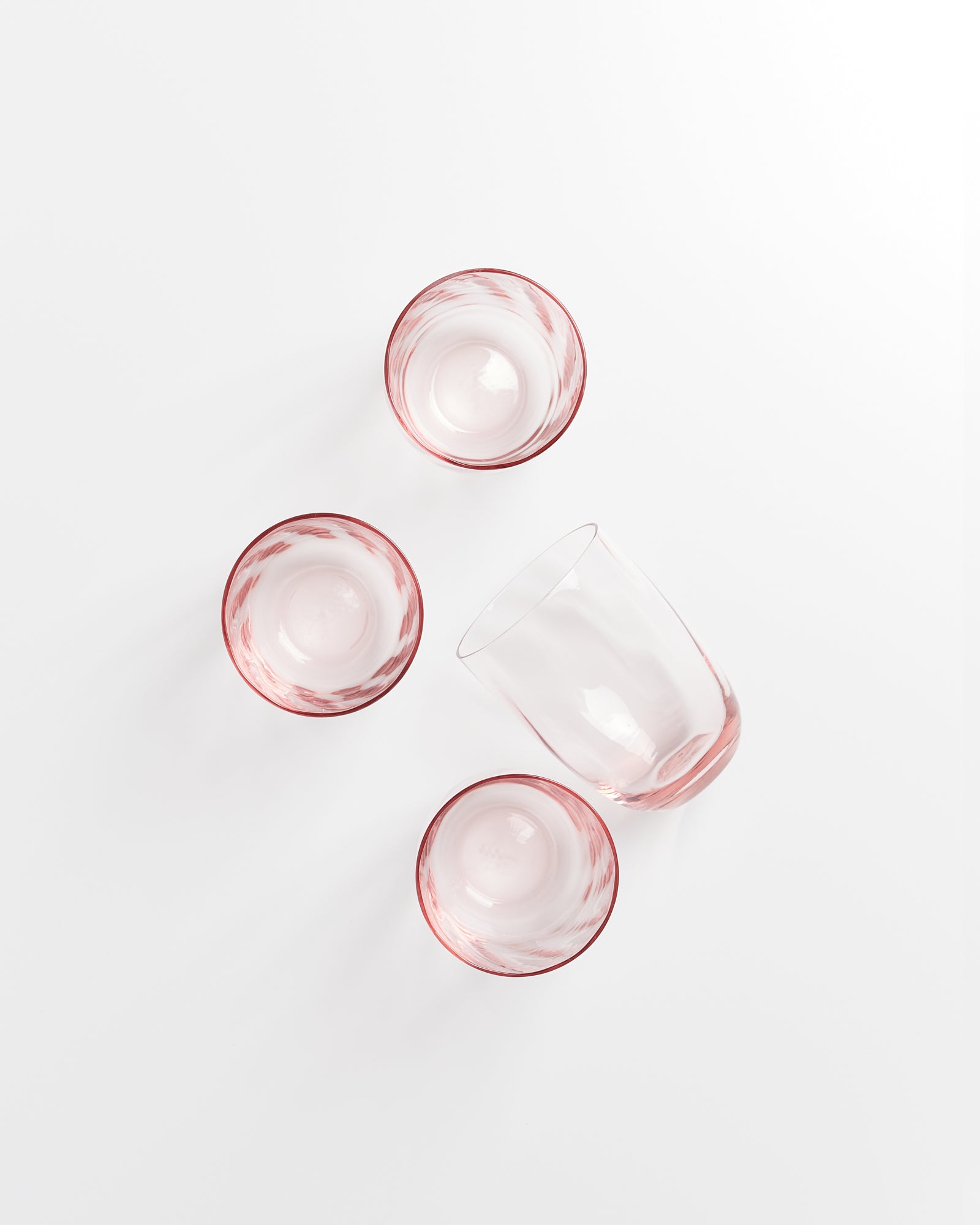 Vier Glasbecher mit rosa Rand auf weißem Hintergrund, einer liegt auf der Seite.