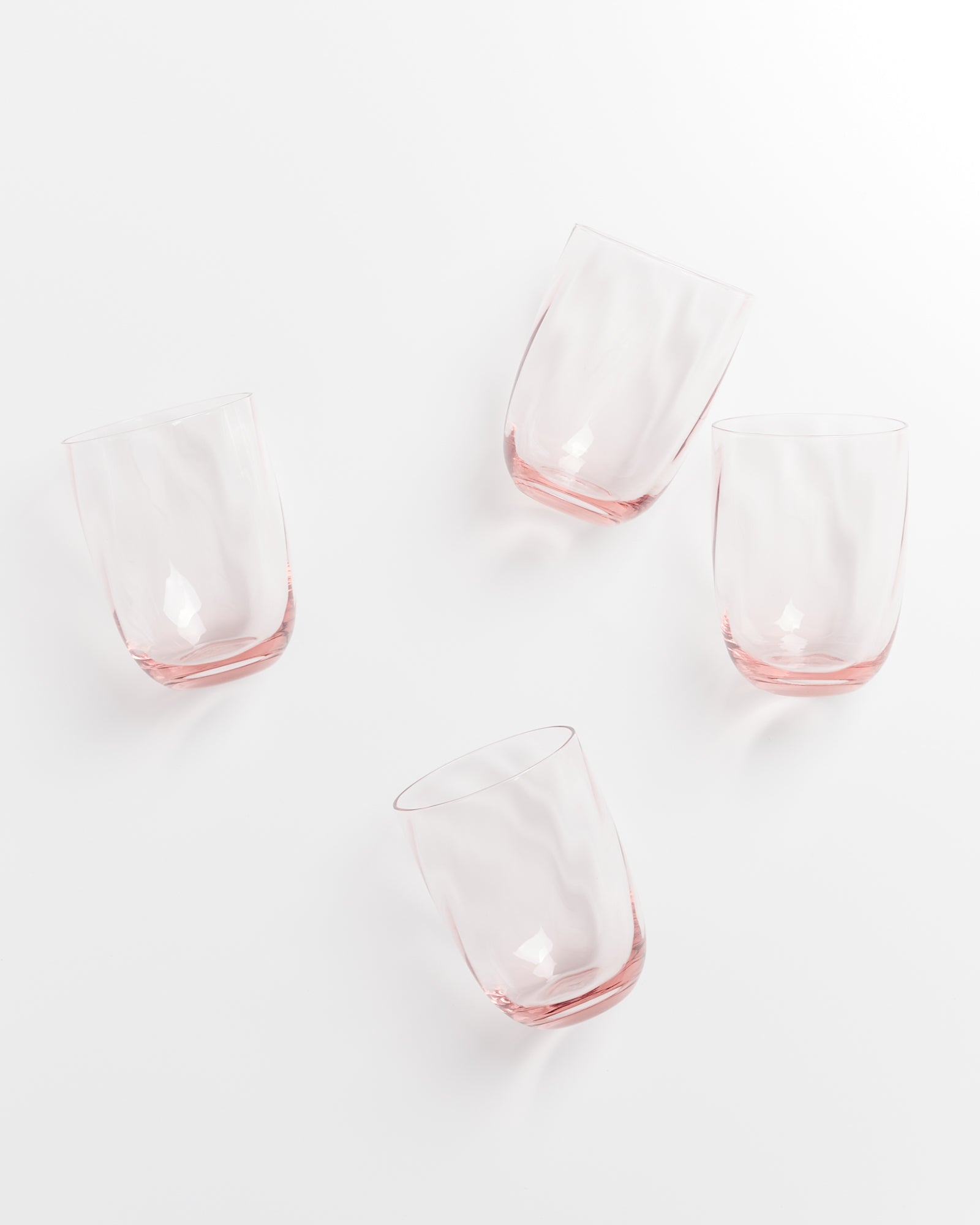 Vier rosafarbene Trinkgläser liegen verstreut auf einem weißen Hintergrund.