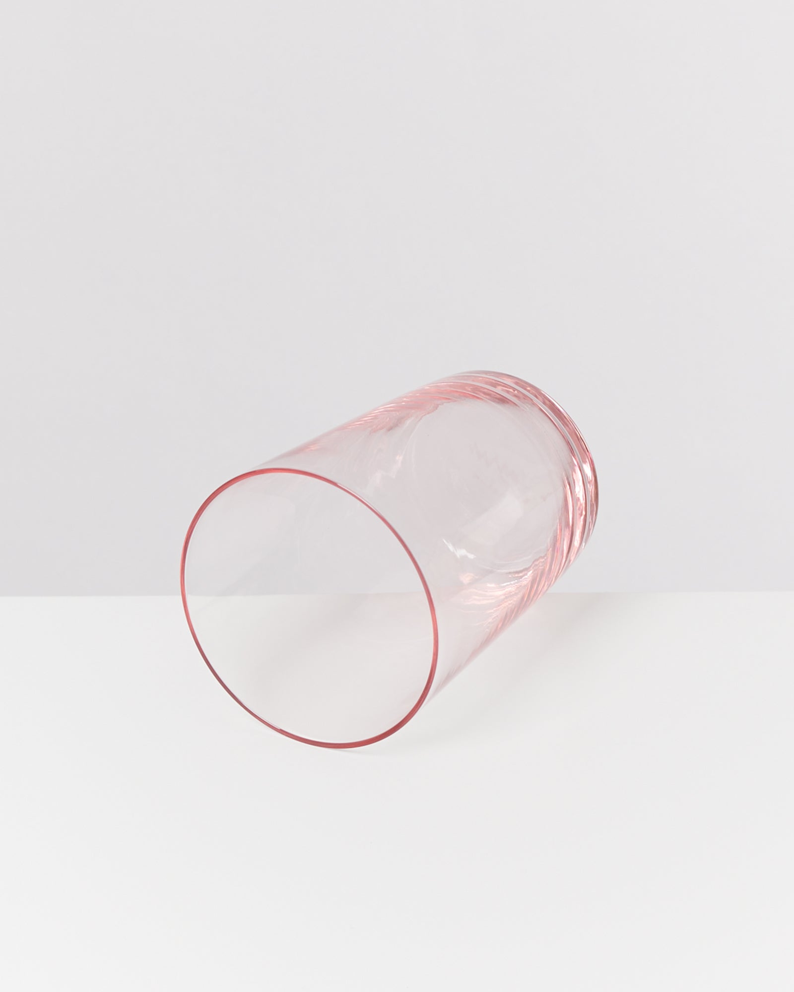 Ein durchsichtiges rosa Glas liegt auf der Seite auf einer weißen Oberfläche.