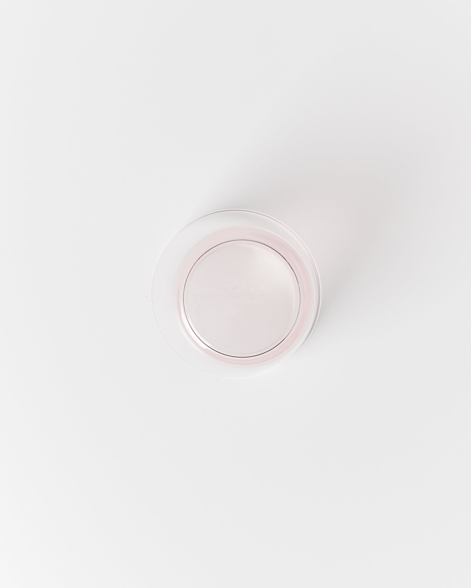 Ein runder, transparenter, rosa Plastikdeckel liegt auf einer weißen Oberfläche.