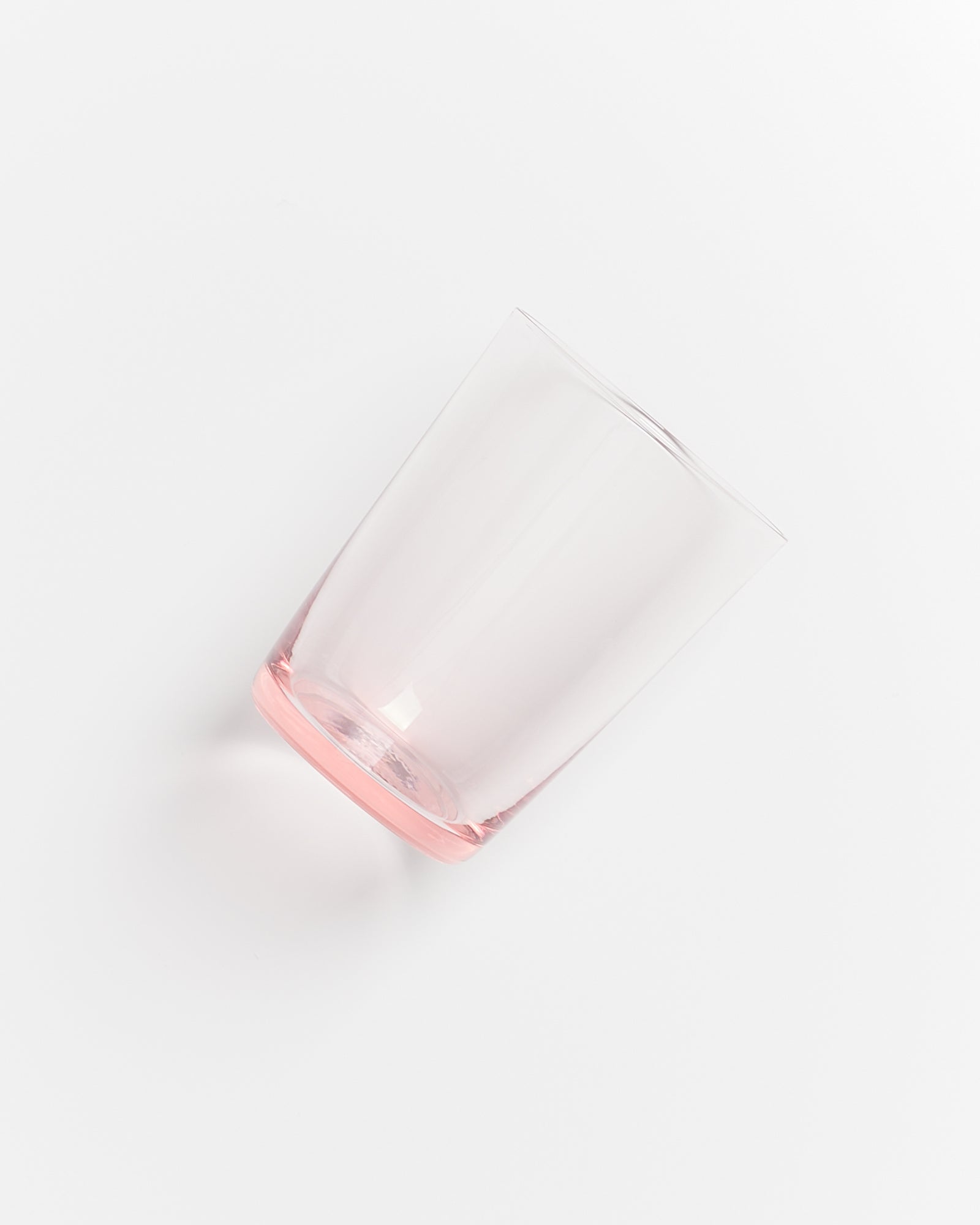 Ein durchsichtiges, leicht rosa getöntes Trinkglas liegt schräg auf einer weißen Oberfläche.