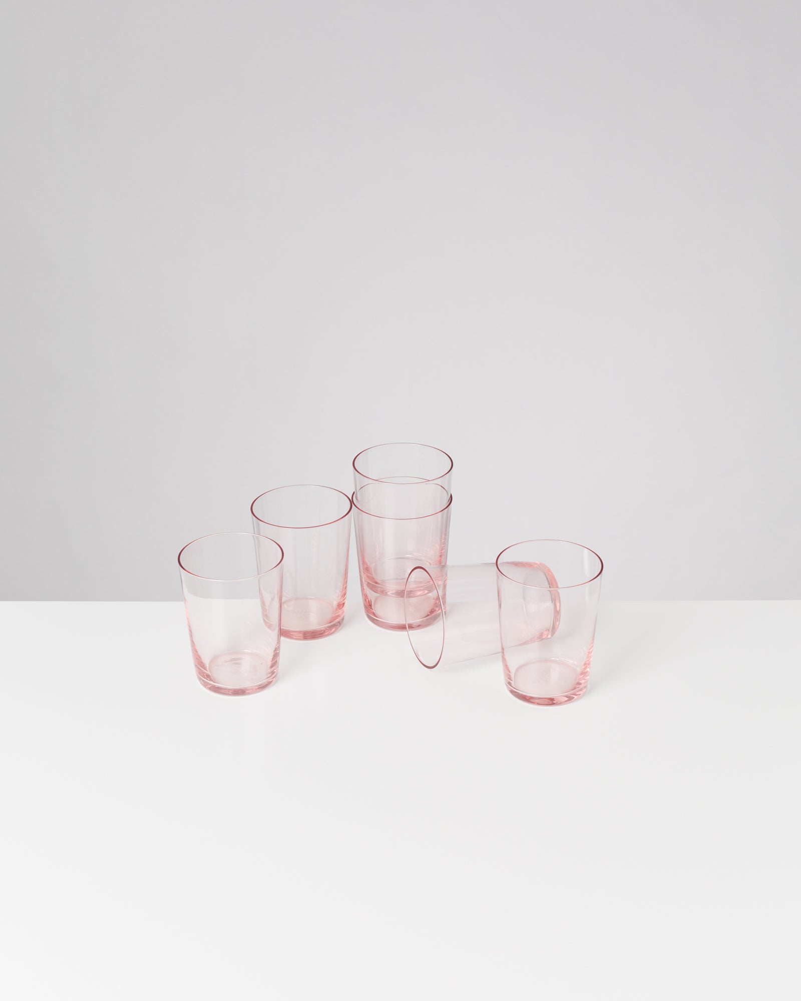 Fünf rosafarbene Gläser auf einem weißen Tisch, eines liegt umgekippt.