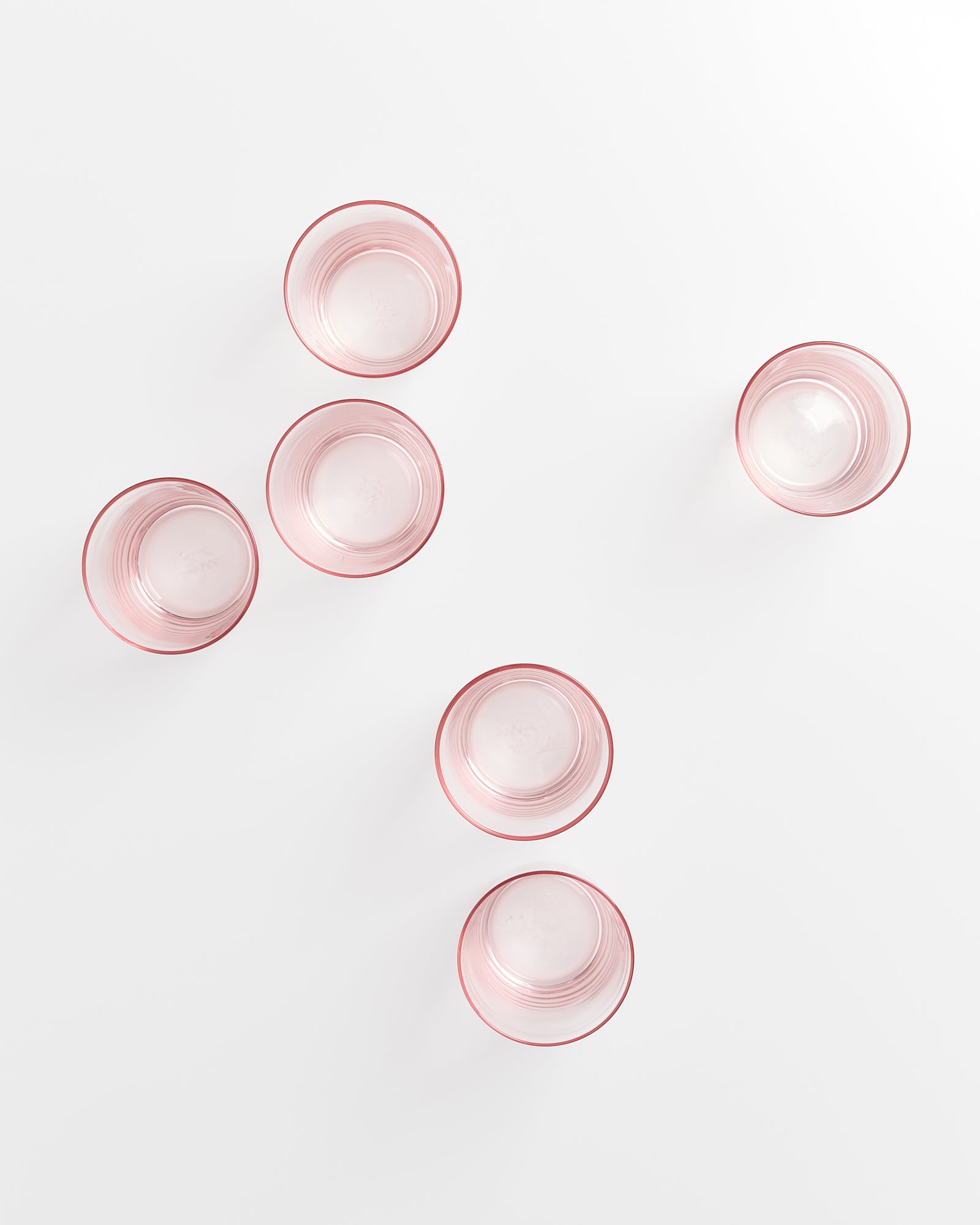Sechs rosafarbene Gläser auf einer weißen Oberfläche aus der Vogelperspektive.