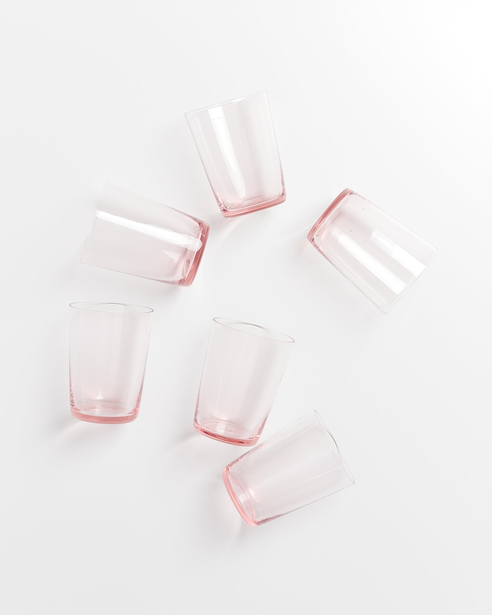 Sechs rosafarbene Trinkbecher liegen lose verteilt auf einer weißen Oberfläche.