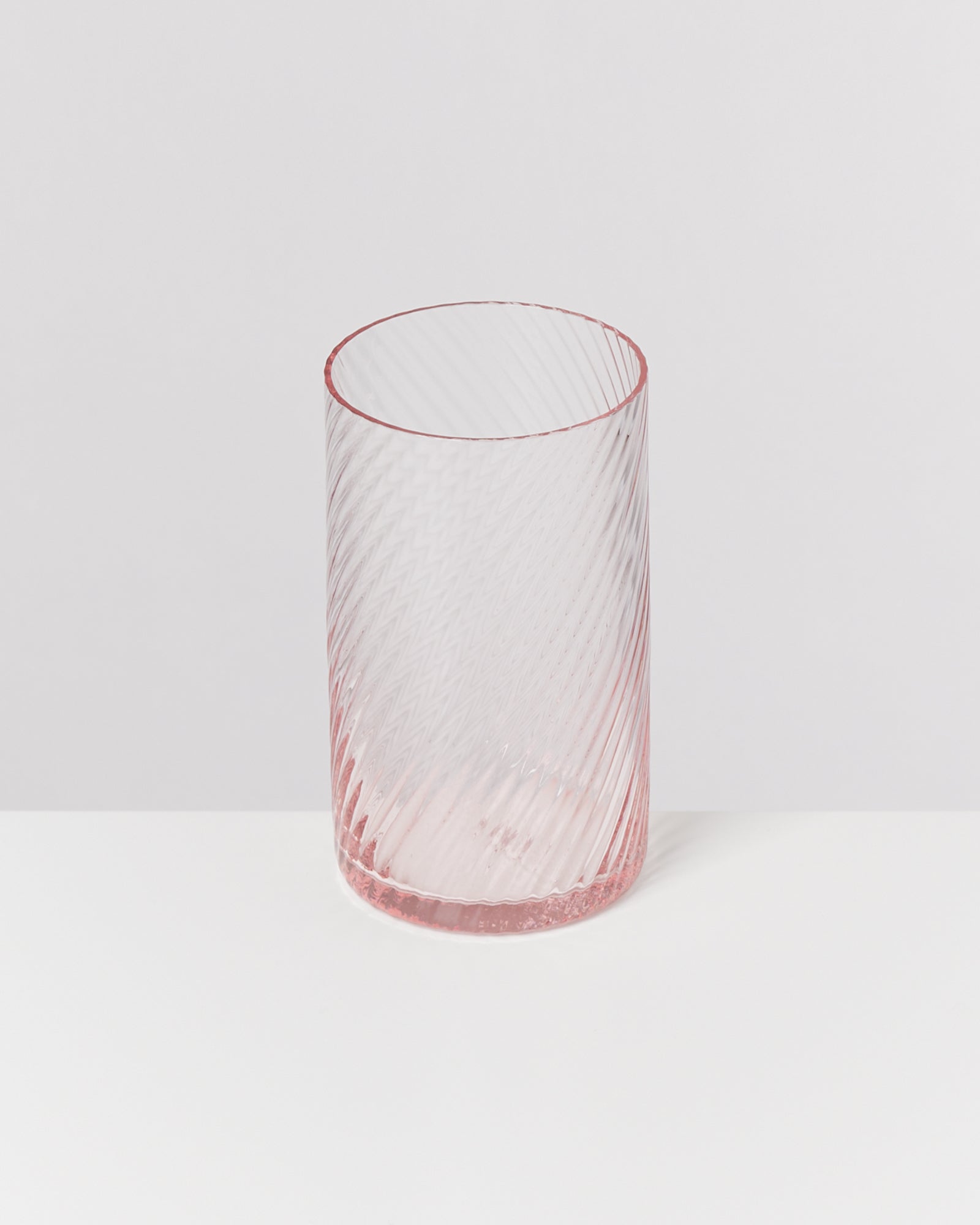 Ein rosafarbenes, geriffeltes Glas steht auf einem weißen Untergrund.