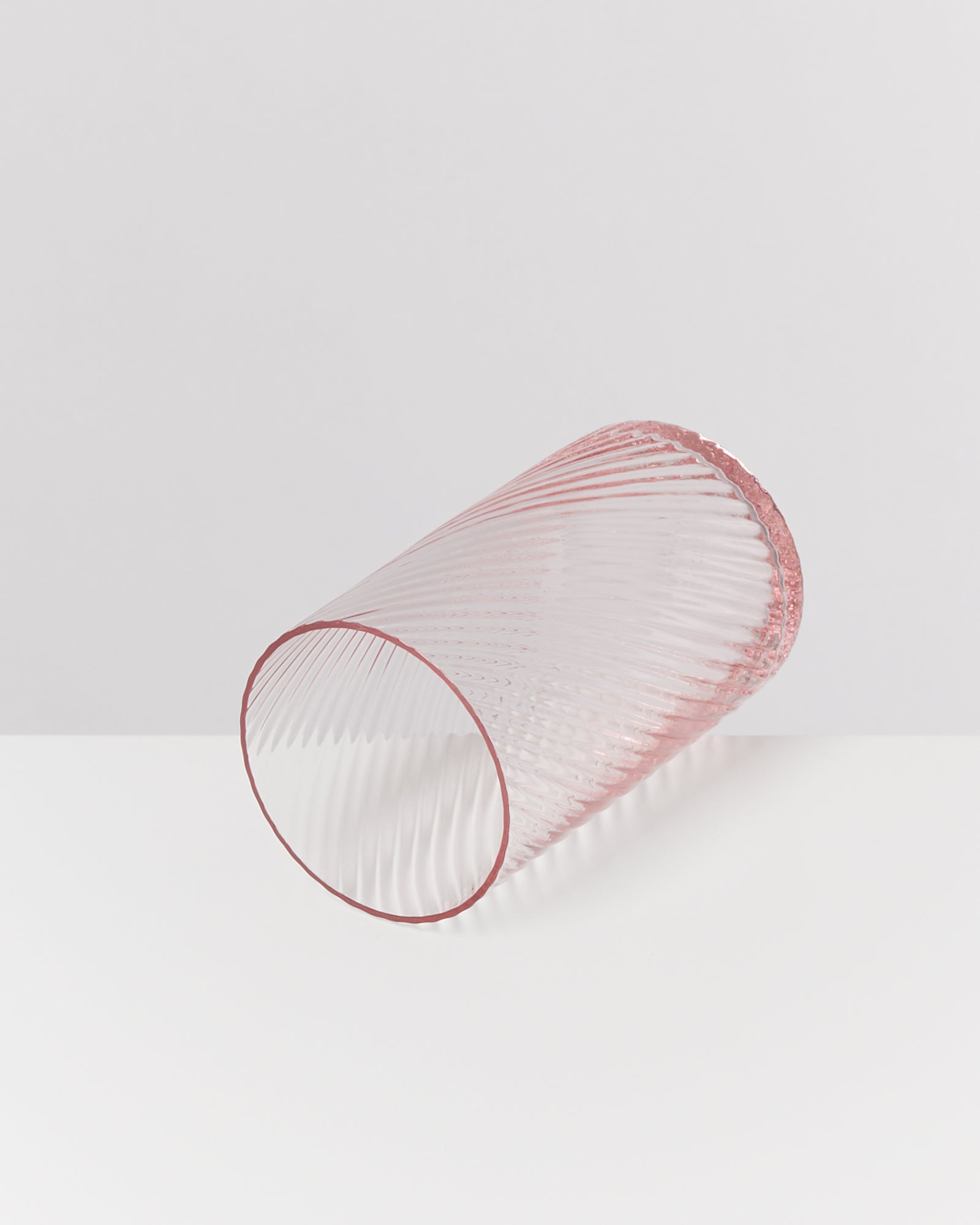 Ein rosafarbener, geriffelter Glasbecher liegt seitlich auf einer hellen Oberfläche.