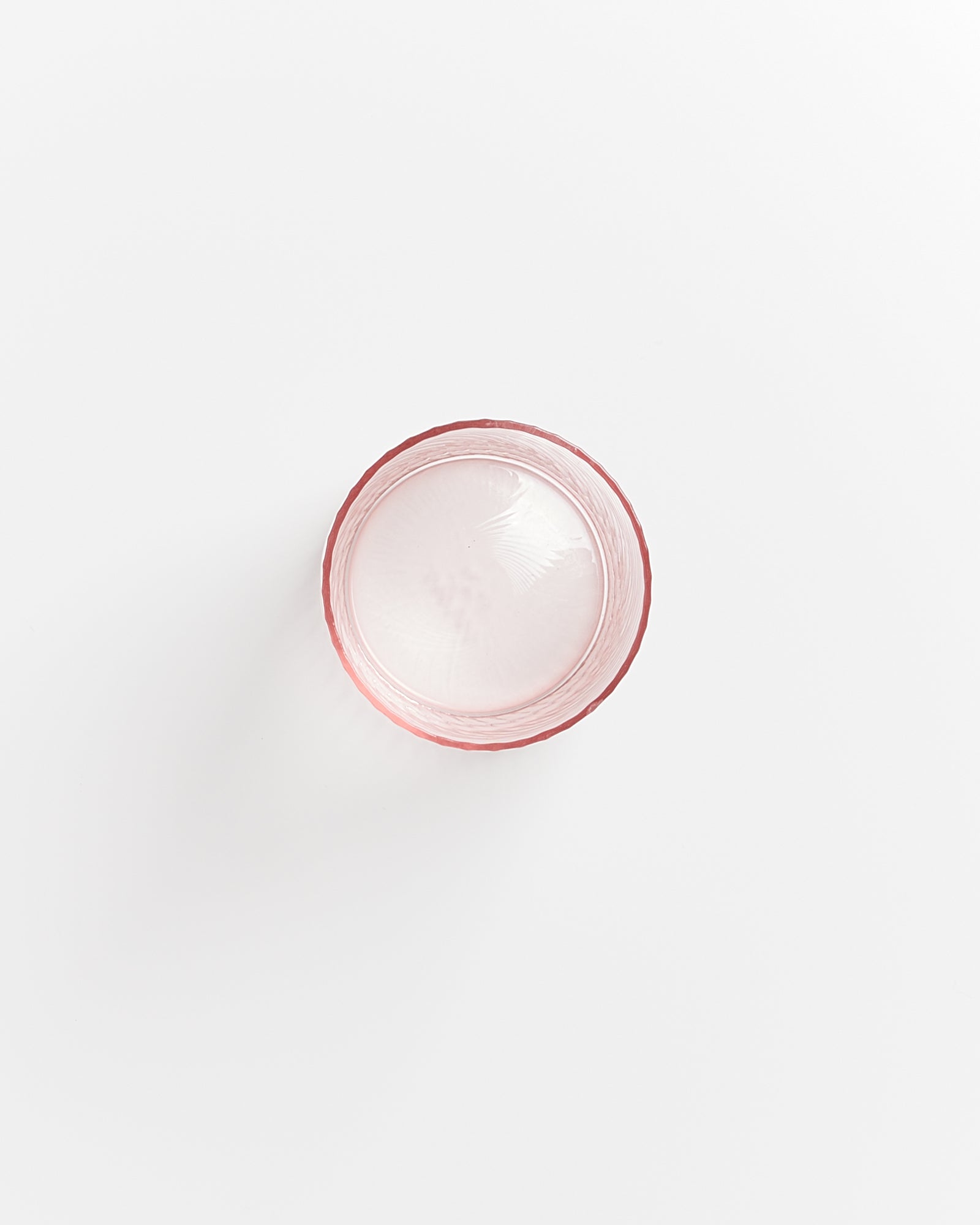 Ein rosa Glas, halb mit Wasser gefüllt, auf weißem Hintergrund von oben gesehen.
