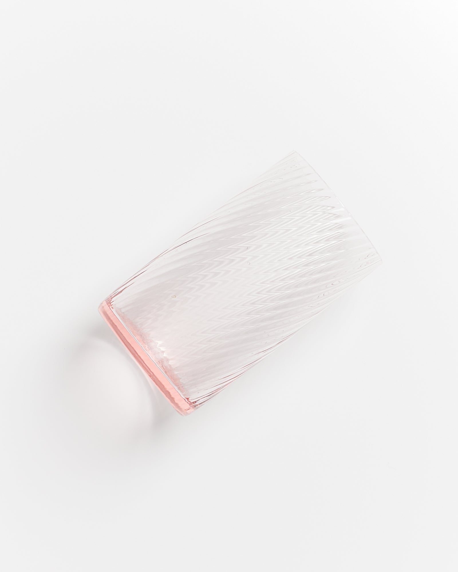 Ein transparentes Glas mit leichter Riffelung liegt schräg auf einer weißen Oberfläche.