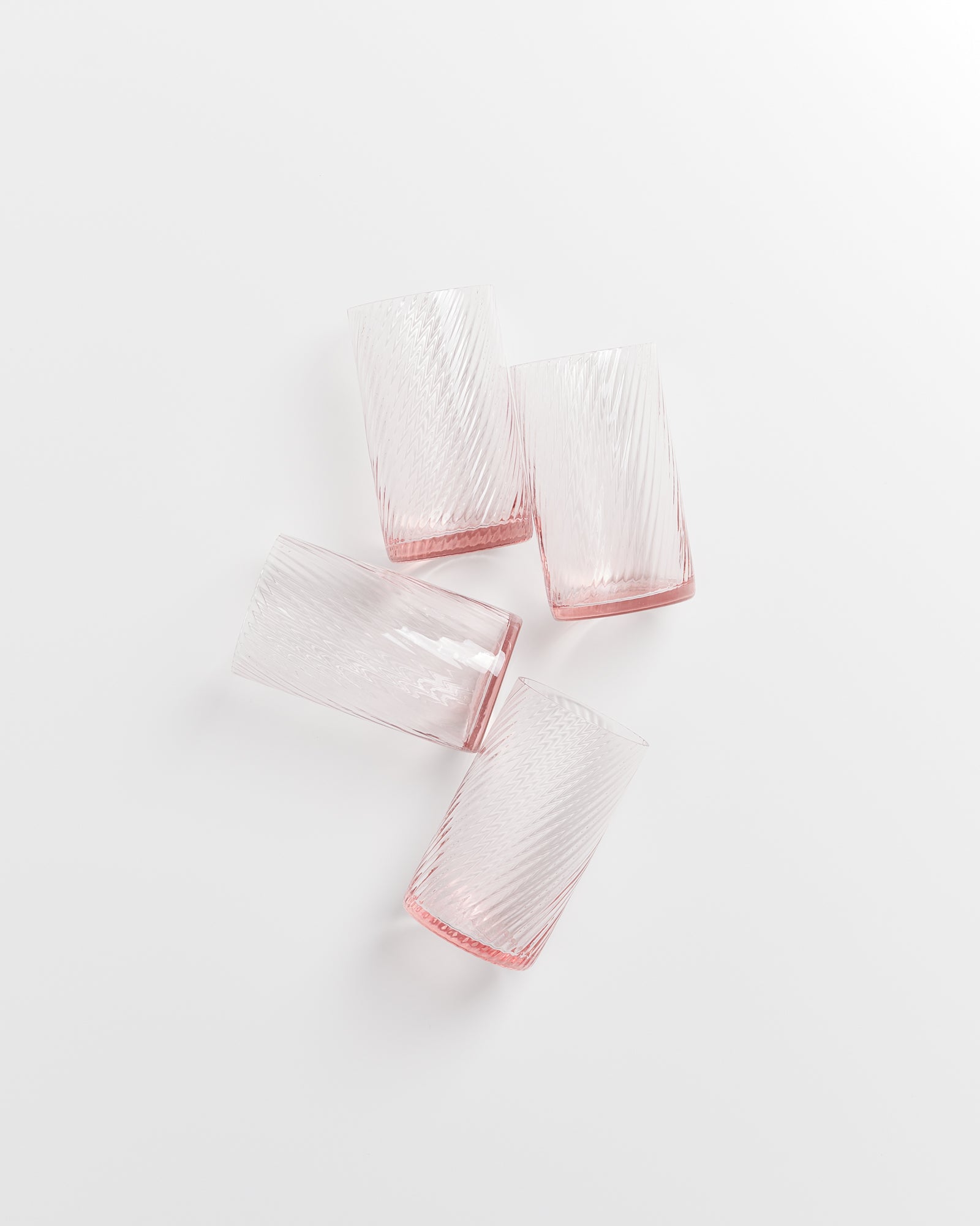 Vier rosafarbene Gläser mit Riffelmuster liegen auf einer weißen Fläche.
