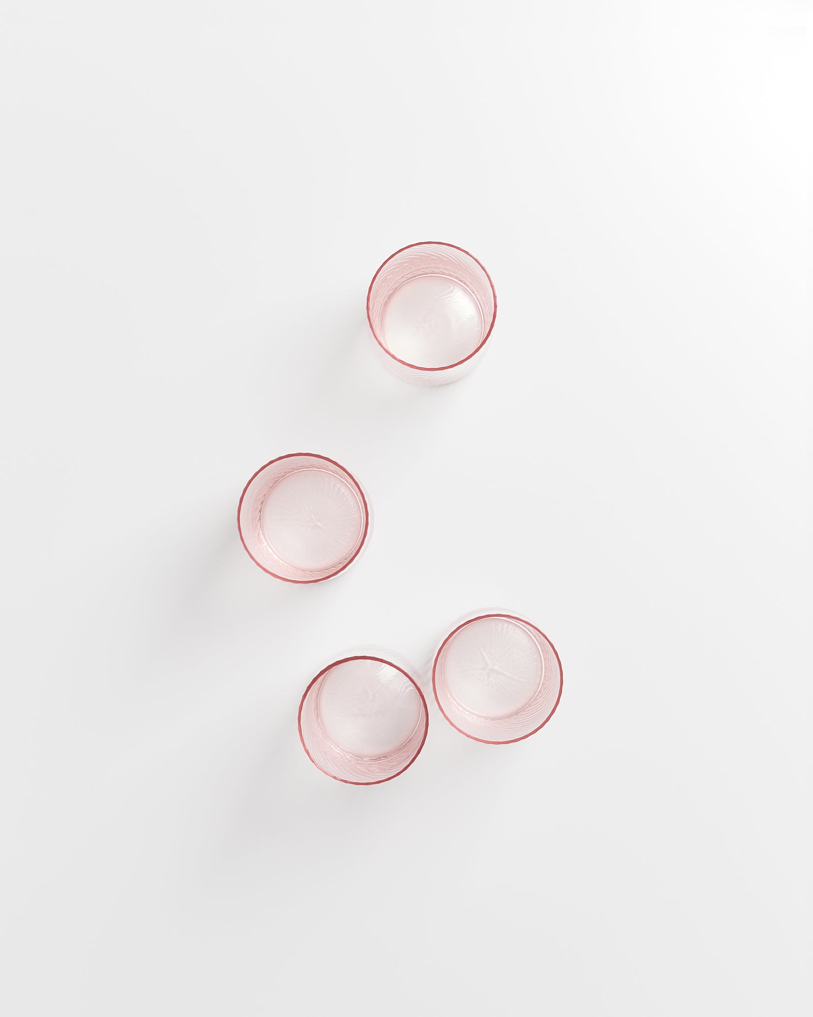 Vier rosafarbene Gläser stehen auf einer weißen Oberfläche.