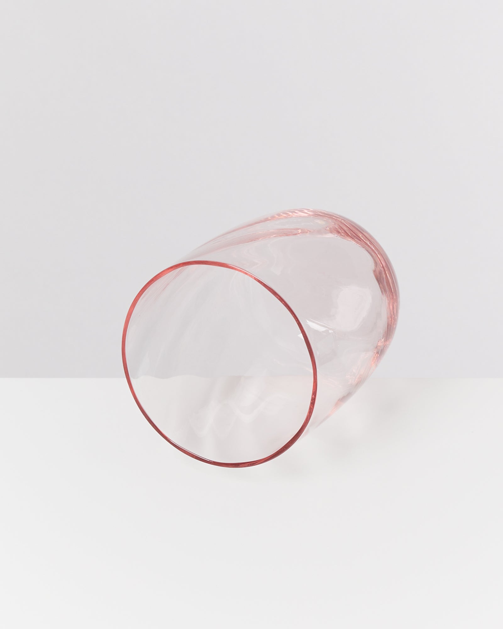 Ein rosafarbenes Glas liegt auf der Seite auf einer weißen Oberfläche vor einem grauen Hintergrund.