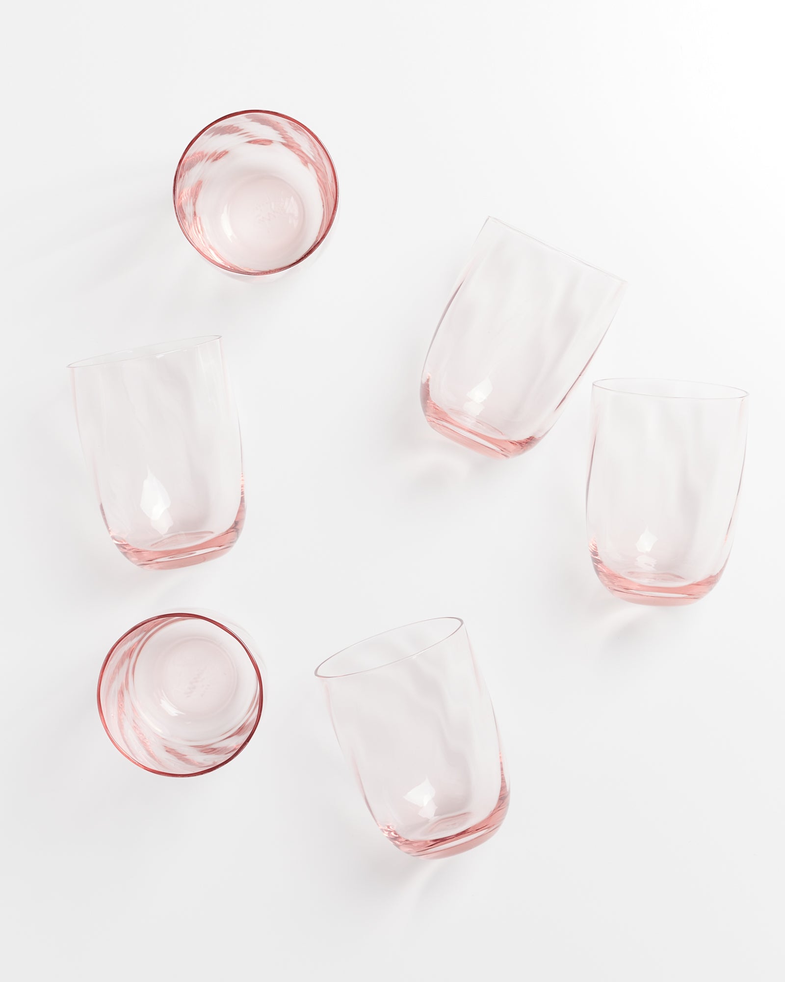 Sechs rosafarbene Gläser liegen und stehen auf einem weißen Hintergrund.