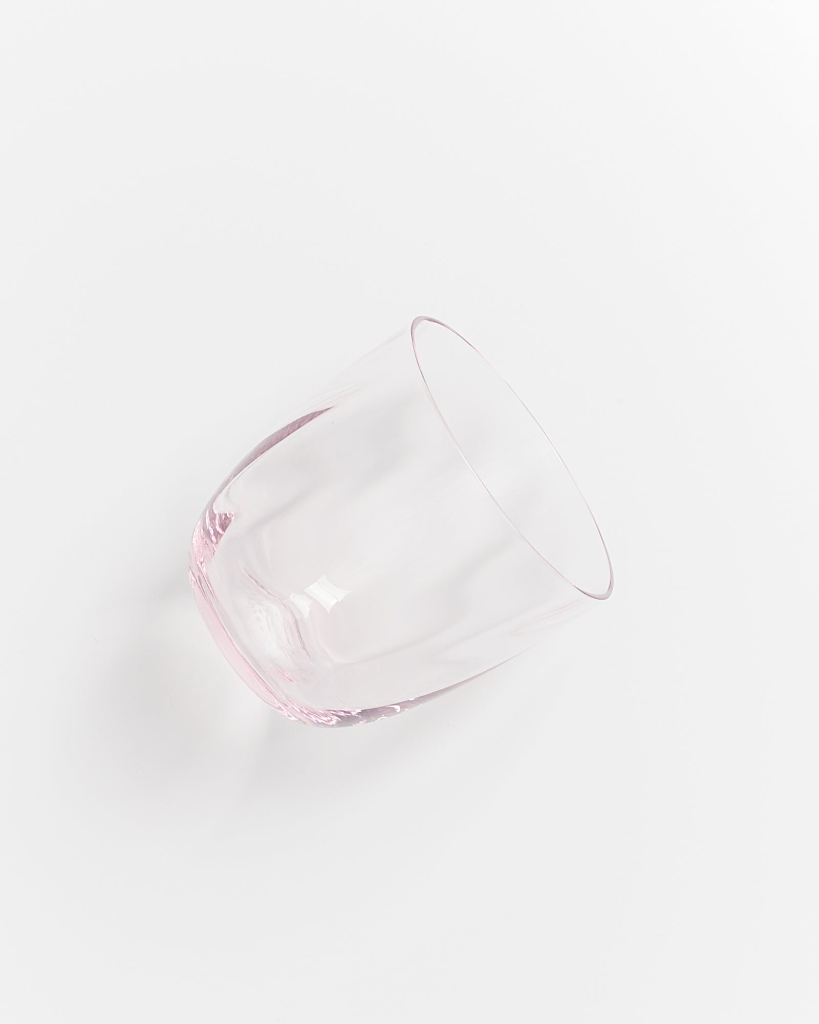 Ein leicht rosafarbenes, schräg liegendes Trinkglas auf weißem Hintergrund.