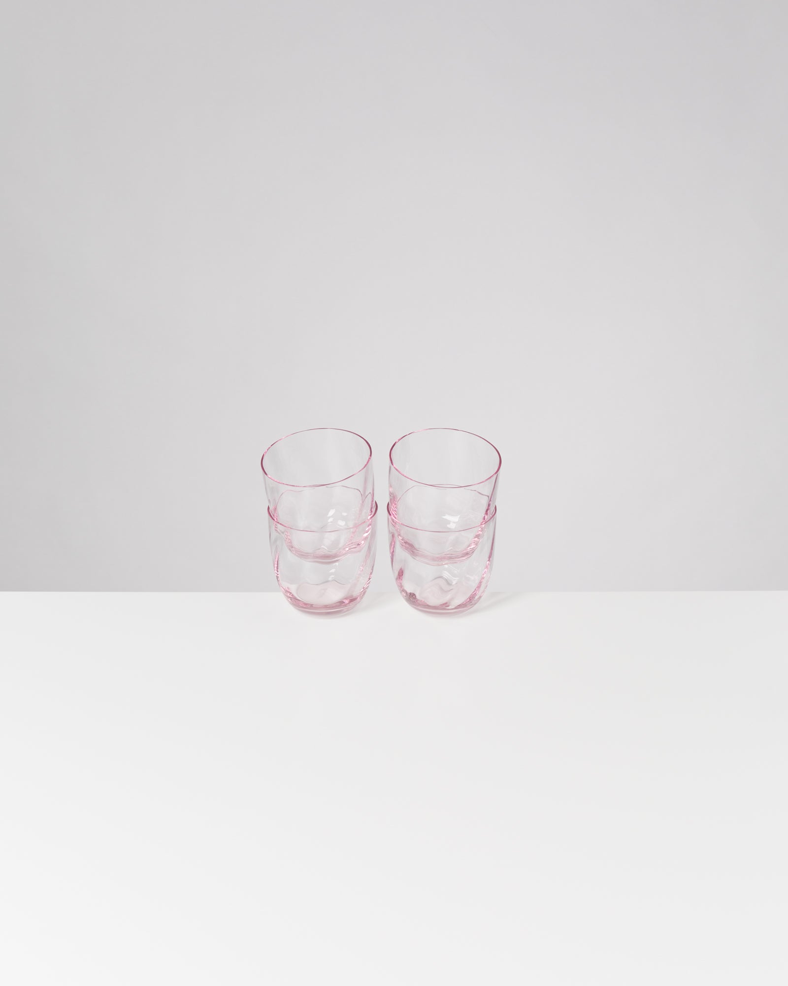 Zwei gestapelte, transparente rosa Gläser auf weißem Tisch vor grauer Wand.