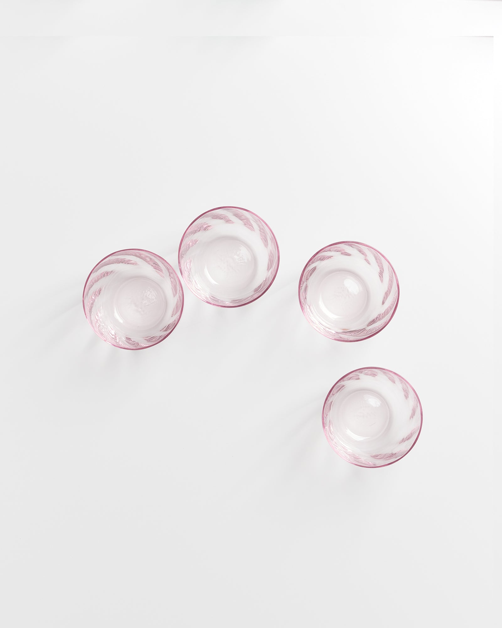 Vier rosafarbene Glasschalen mit weißem Muster stehen auf einem weißen Hintergrund.