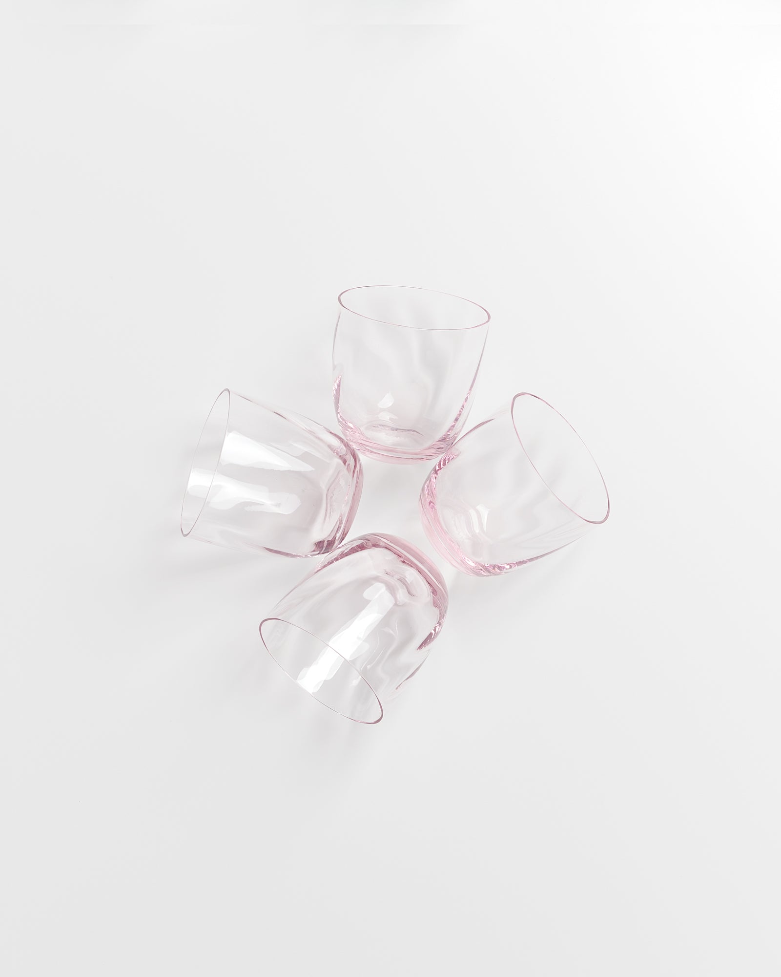 Vier rosafarbene Gläser liegen im Kreis auf einer weißen Oberfläche.