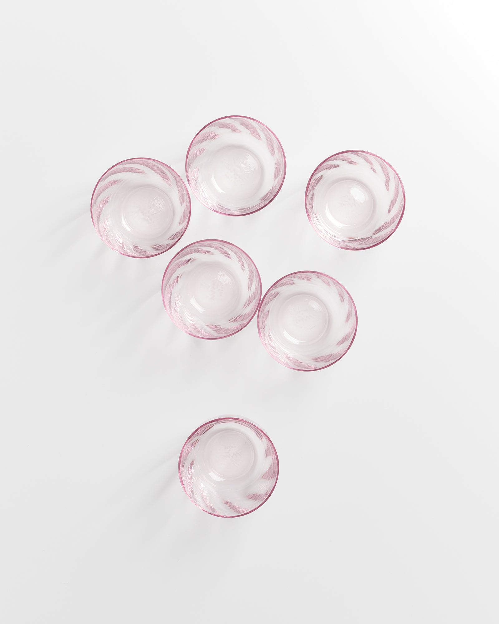 Sechs rosa Glasbecher mit dekorativen Mustern, von oben betrachtet, auf einer weißen Oberfläche angeordnet.