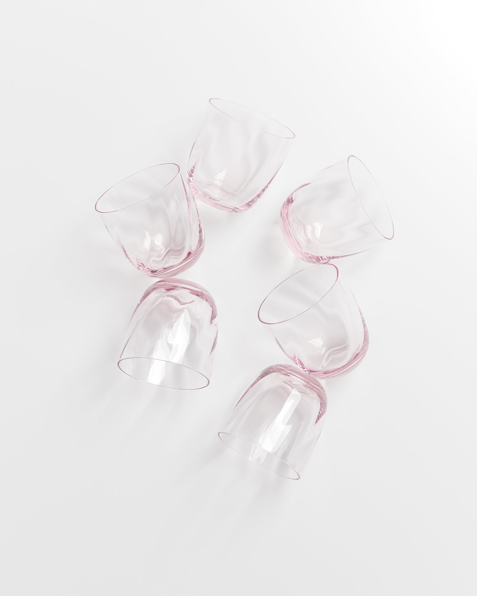 Sechs rosa Gläser liegen auf einer weißen Oberfläche durcheinander verstreut.
