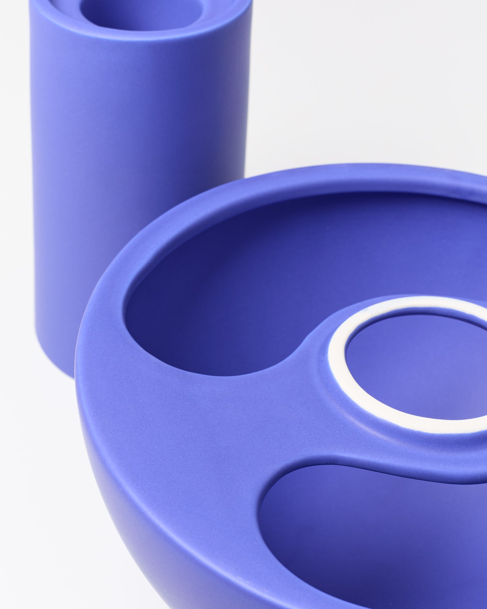 Zwei abstrakte, violette Kunststoffformen, eine zylindrisch und die andere rund, mit Löchern auf weißem Hintergrund.