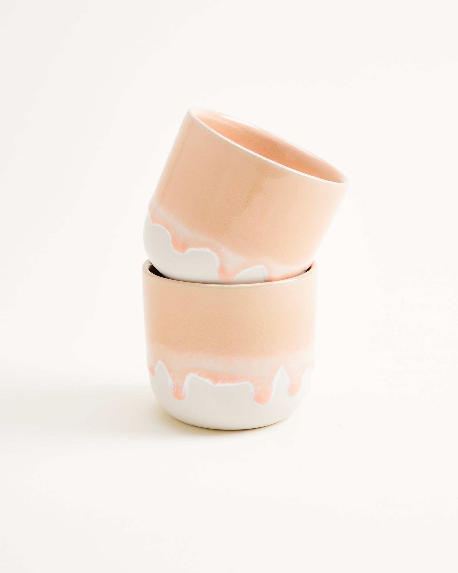Zwei übereinander gestapelte Keramikbecher mit pastellfarbenem, tropfendem Design auf weißem Hintergrund.